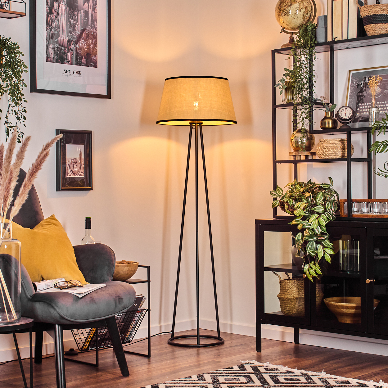 Ein Raum mit Stehlampe, Sessel und schwarzem Regal. Die Einrichtung umfasst Kunstwerke, Pflanzen und Dekorationsartikel. Auf dem Boden liegt ein Teppich.