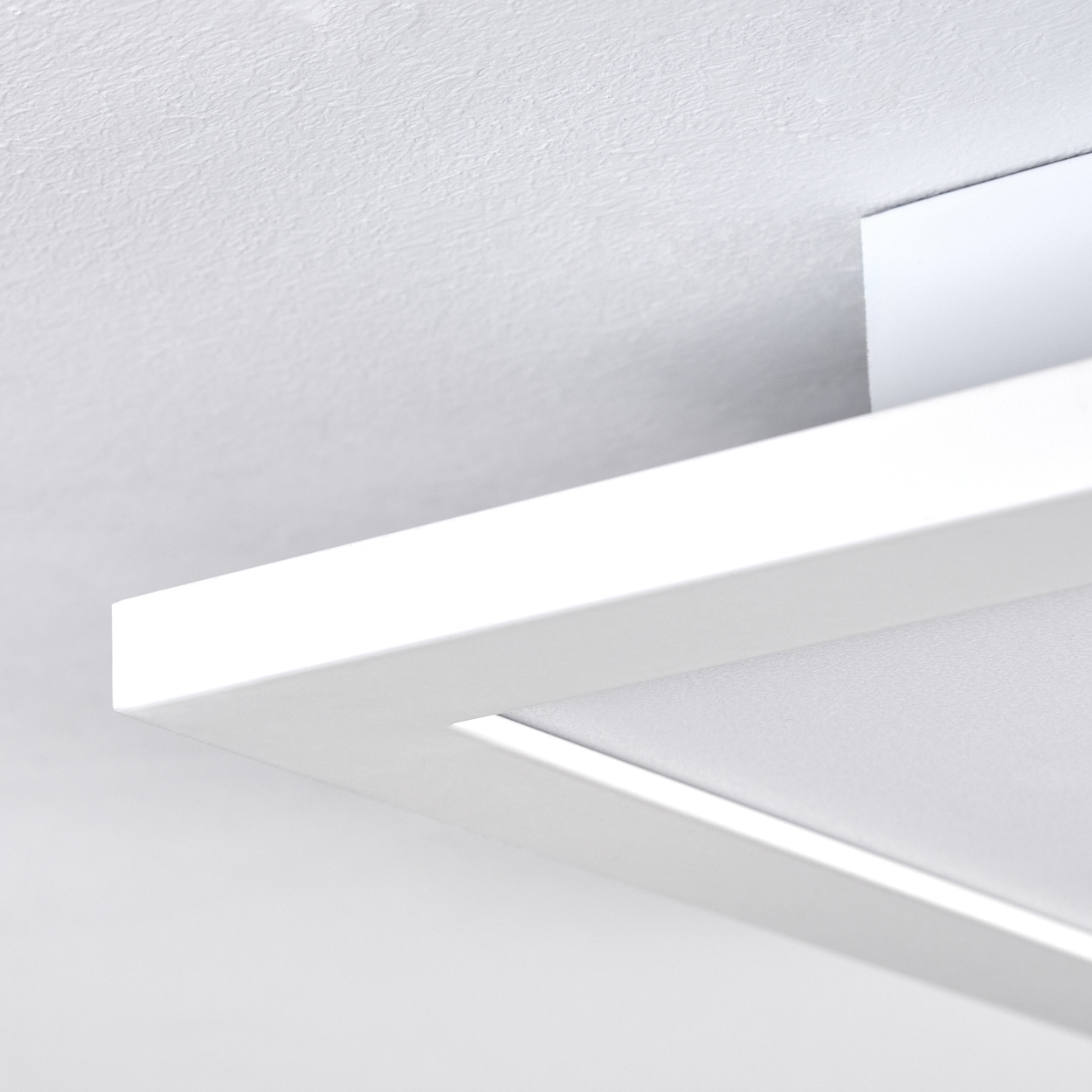 Nahaufnahme einer weißen Deckenleuchte. Die Leuchte ist rechteckig mit einem eingelassenen Licht. Der Hintergrund ist eine weiße Decke.
