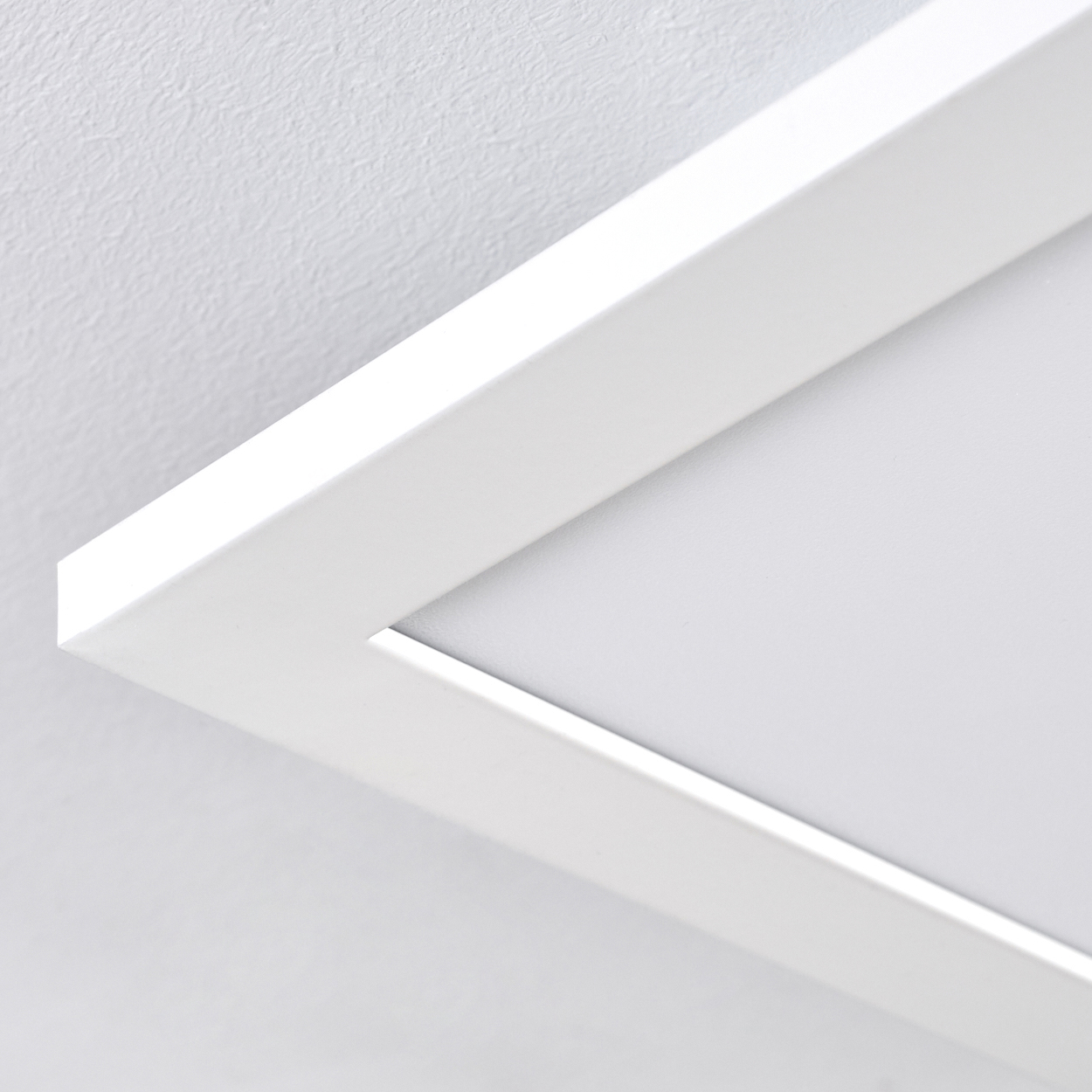 Nahaufnahme einer weißen, rechteckigen Deckenleuchte. Der Rahmen ist weiß, der Hintergrund ist eine weiße Decke.