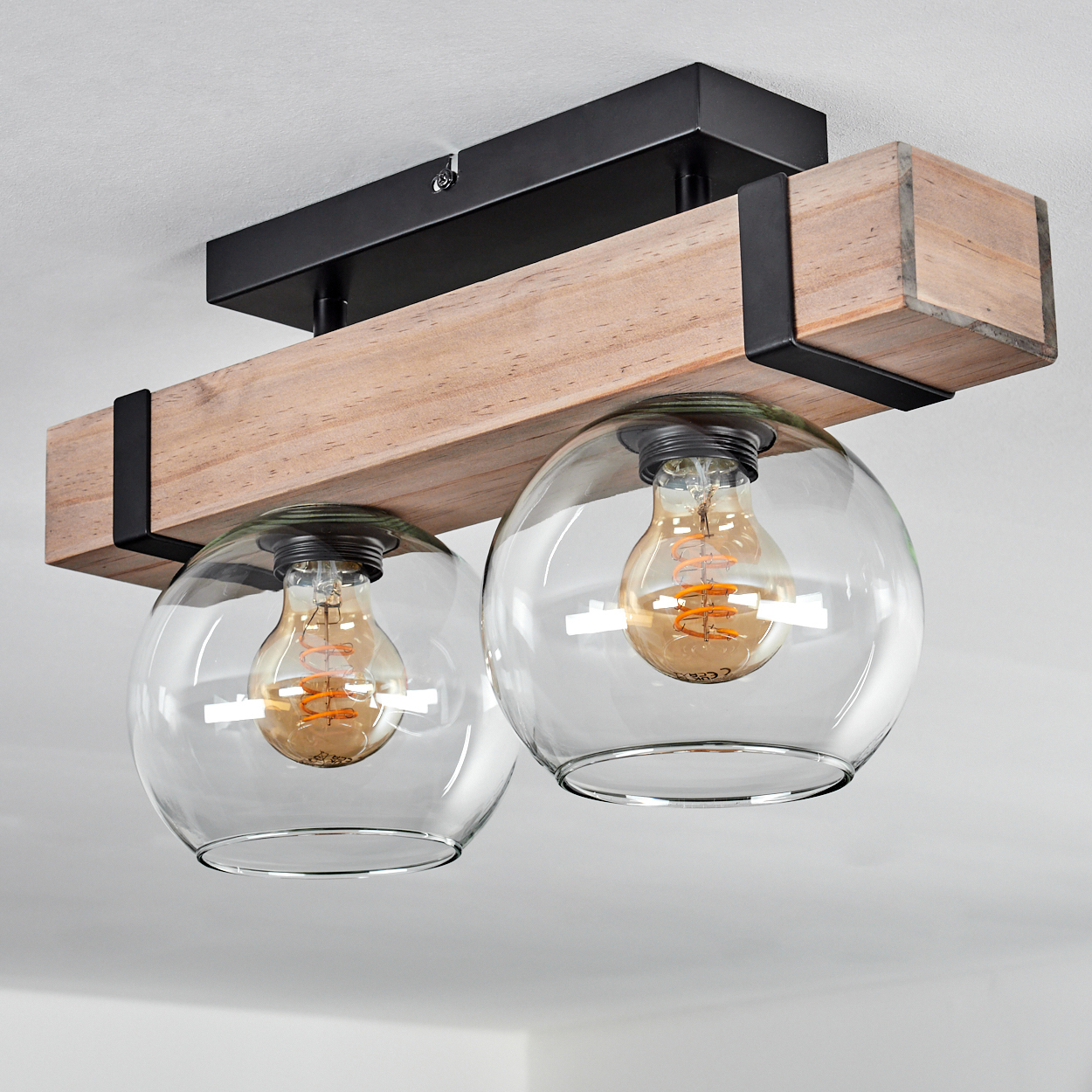 Deckenleuchte mit zwei klaren Glaskugeln, Holzbalken und schwarzen Metallakzenten. Jede Kugel enthält eine sichtbare Glühbirne.