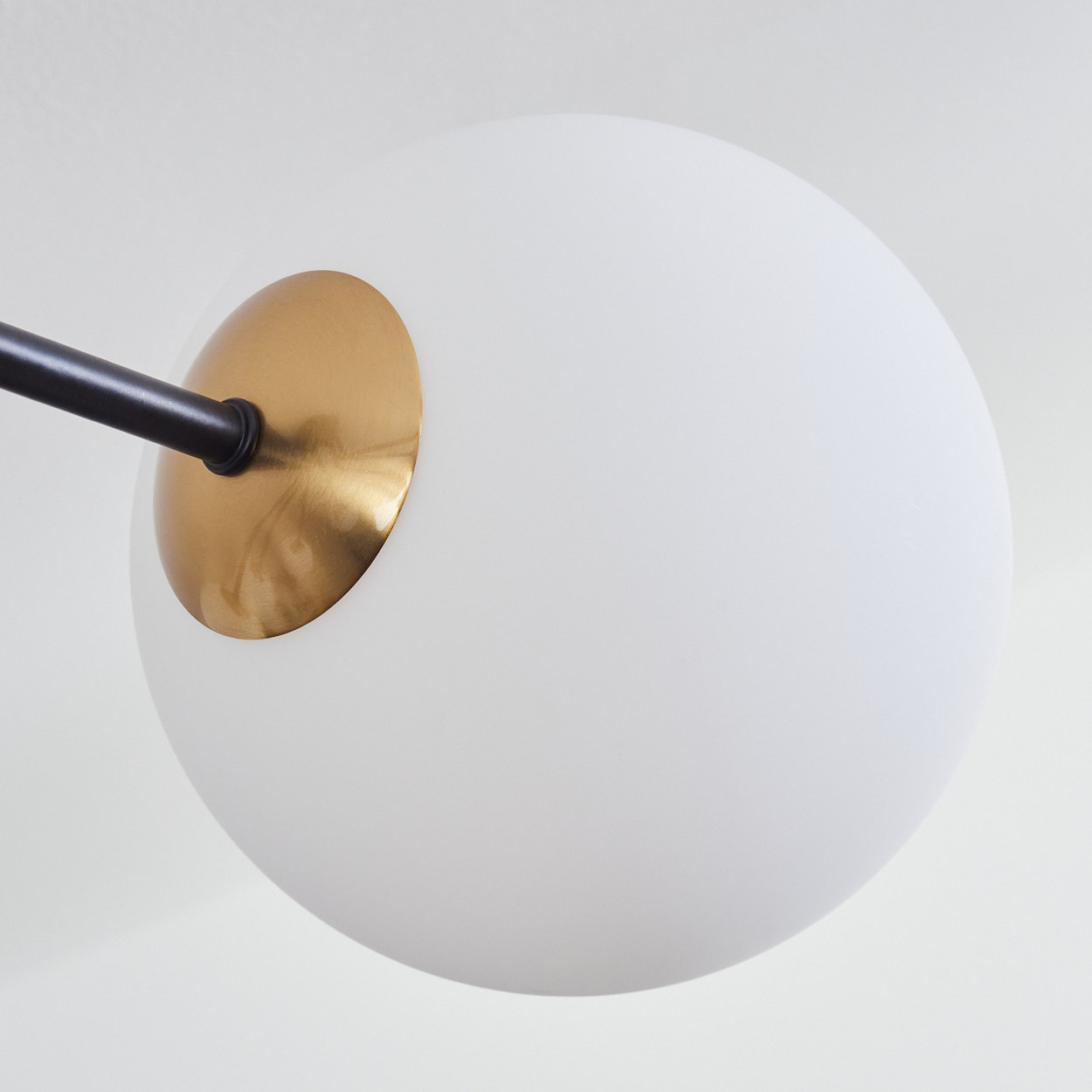 Nahaufnahme einer modernen Lampe. Sie hat eine weiße Kugel, einen goldfarbenen Sockel und einen schwarzen Arm vor weißem Hintergrund.