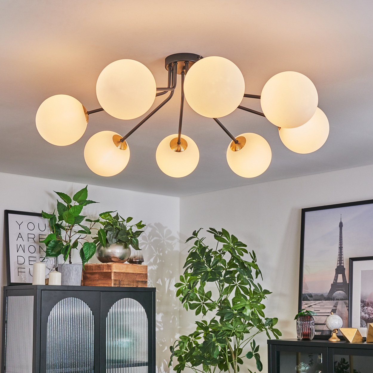 Eine moderne Deckenleuchte mit kugelförmigen Lampen. Innenszene mit Pflanzen, Kunst und einem schwarzen Schrank.