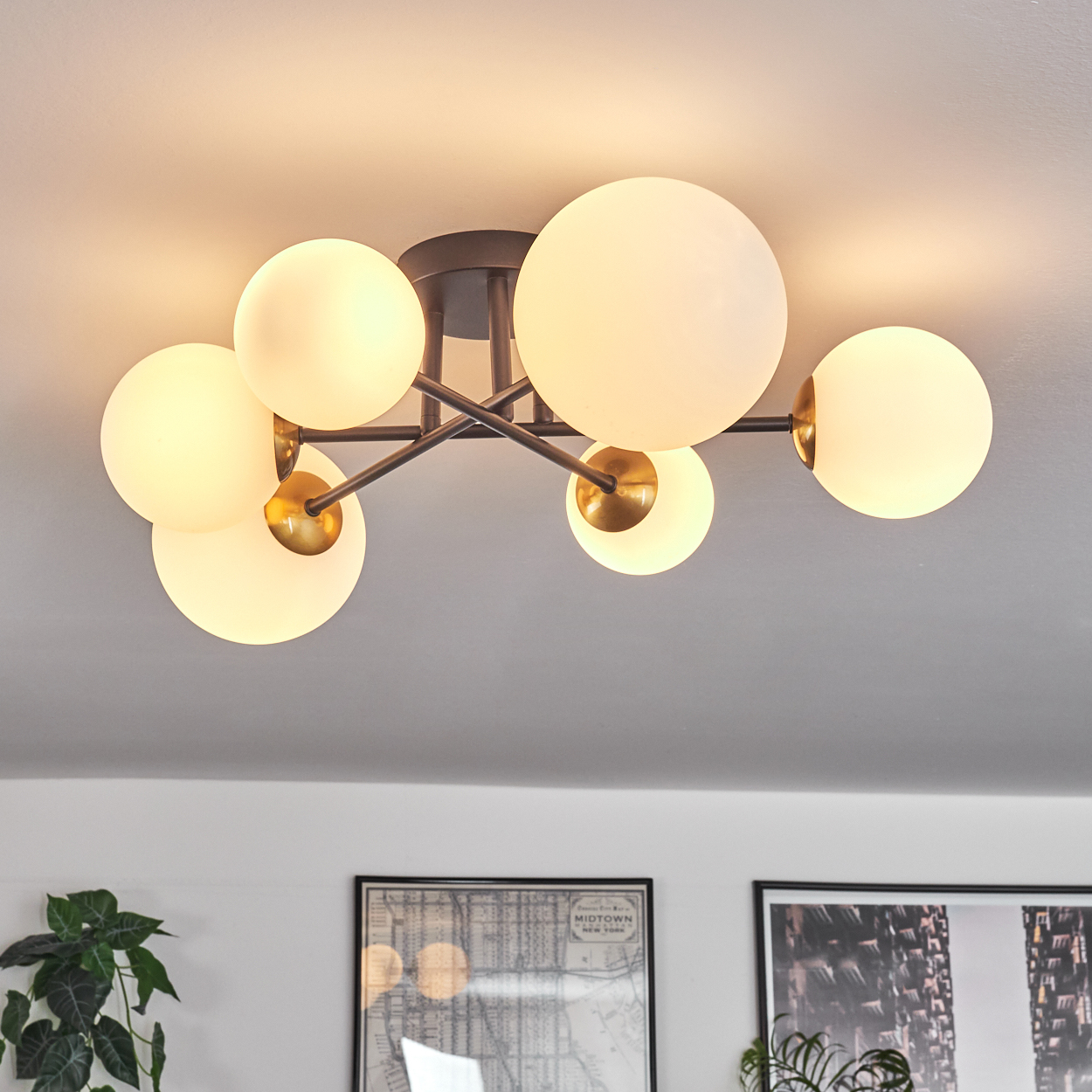 Eine moderne Deckenleuchte mit sechs kugelförmigen, mattierten Glasschirmen. Die Leuchte hat einen dunklen Metallrahmen mit goldenen Akzenten. Im Hintergrund sieht man eine weiße Decke.