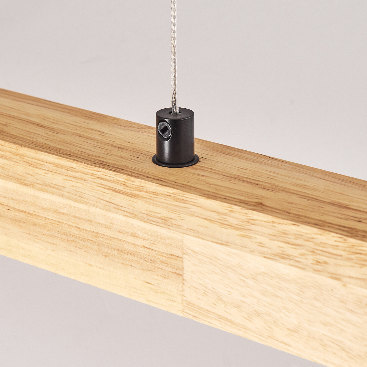Ein Holzbalken mit einem schwarzen Metallzylinder. Ein silberner Draht erstreckt sich vom Zylinder. Der Hintergrund ist schlicht weiß.