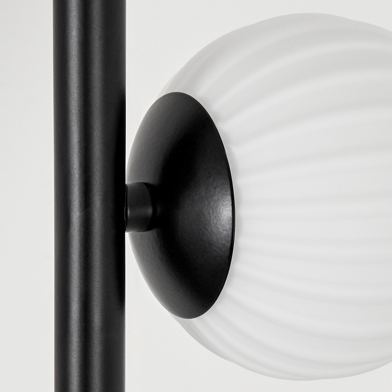 Nahaufnahme einer modernen Lampe. Sie hat einen schwarzen Metallrahmen und eine weiße, gerippte Glaskugel. Der Hintergrund ist weiß.