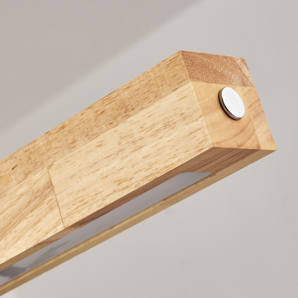 Nahaufnahme eines Holzbalkens mit Lichtleiste. Am Ende befindet sich eine silberne Scheibe. Der Hintergrund ist hellgrau.