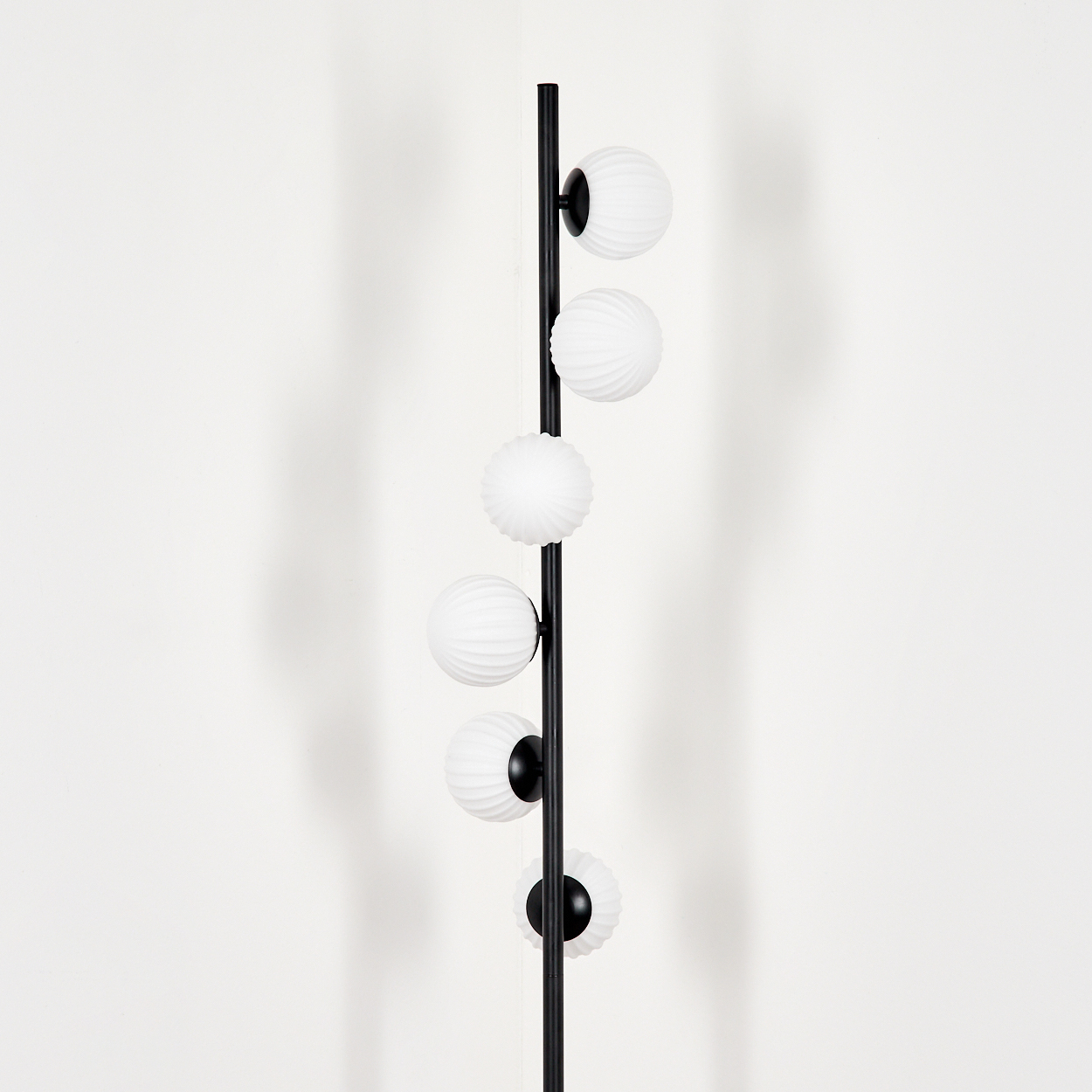 Eine schwarze Stehlampe mit sechs weißen, kugelförmigen Lampenschirmen. Der Hintergrund ist eine weiße Wand.