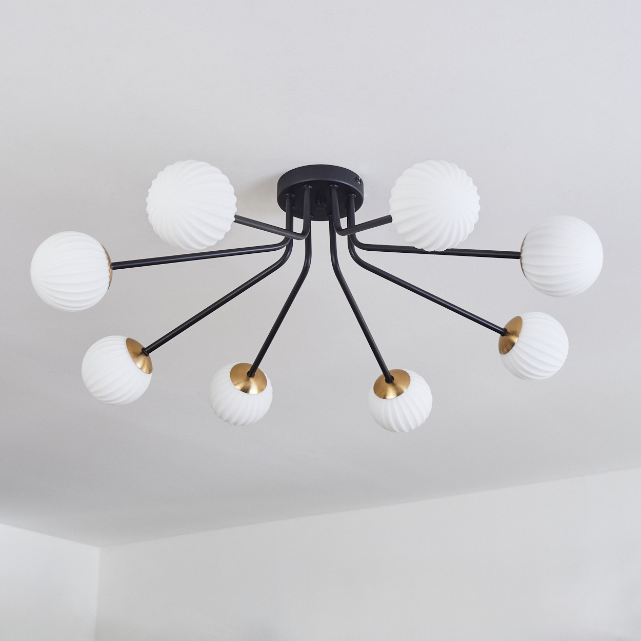 Eine moderne Deckenleuchte mit acht weißen Kugelschirmen, schwarzen Armen und goldenen Akzenten, an einer weißen Decke montiert.