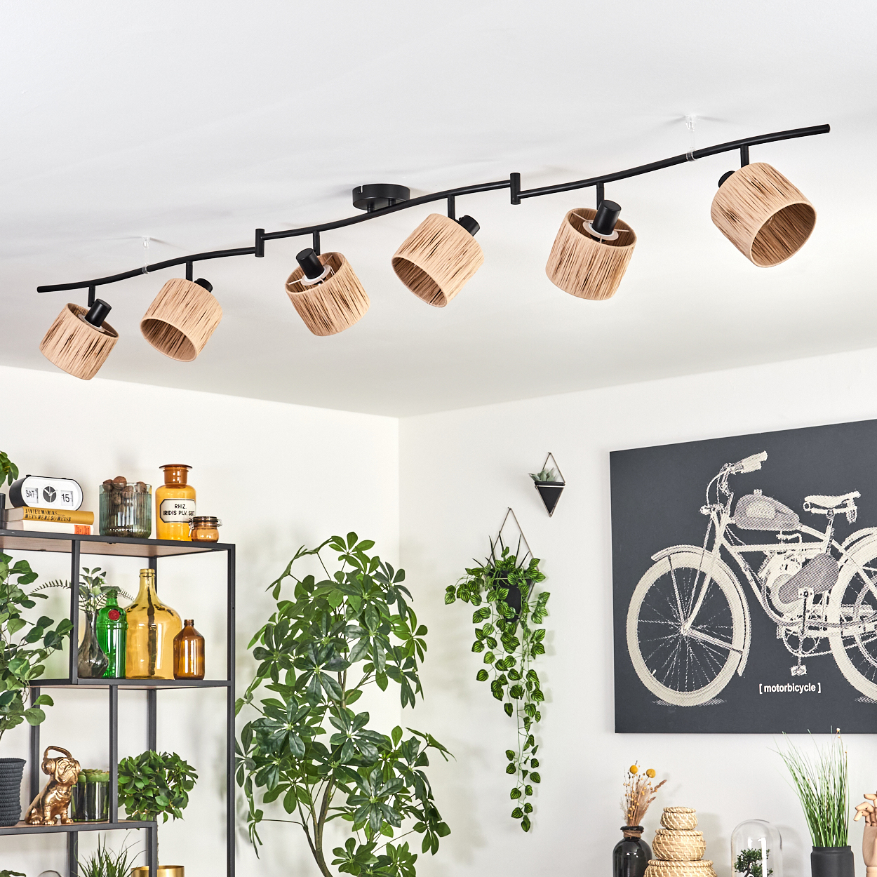 Eine moderne Deckenleuchte mit sechs Lampenschirmen aus gewebtem Material. Die Szene umfasst Pflanzen, ein Regal mit Gegenständen und Motorradkunst.
