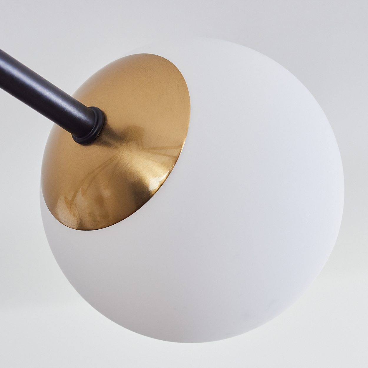 Eine moderne Leuchte mit weißem Globus, goldfarbener Oberseite und schwarzem Arm. Der Hintergrund ist schlicht weiß.
