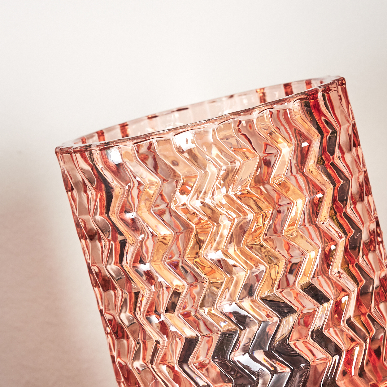 Nahaufnahme einer rosa Glasvase mit Zickzackmuster. Die Vase ist geneigt, mit hellem Hintergrund. Das Glas reflektiert Licht.