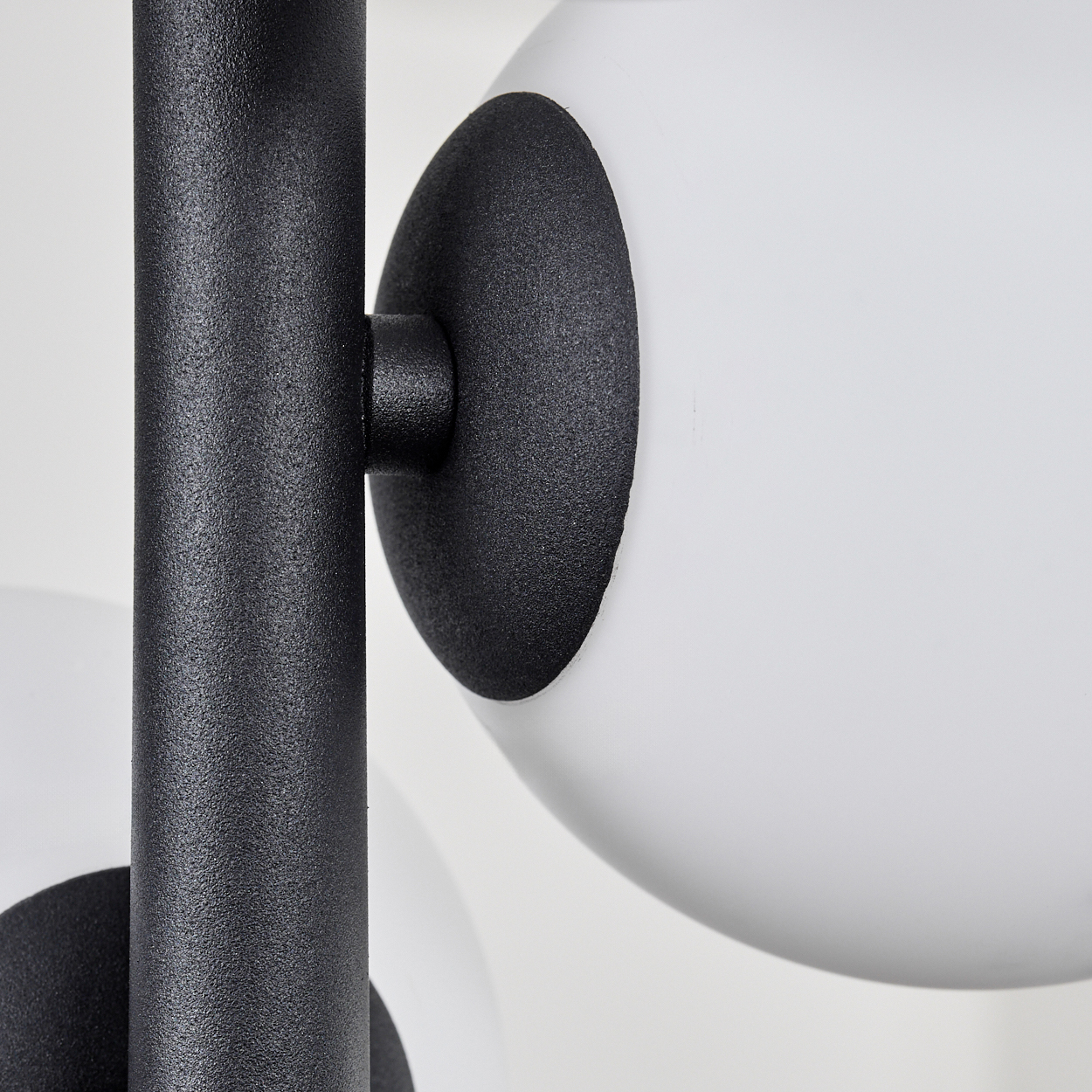 Nahaufnahme einer modernen Lampe mit schwarzem Metallrahmen und weißen, kugelförmigen Lichtern. Der Hintergrund ist schlicht weiß.