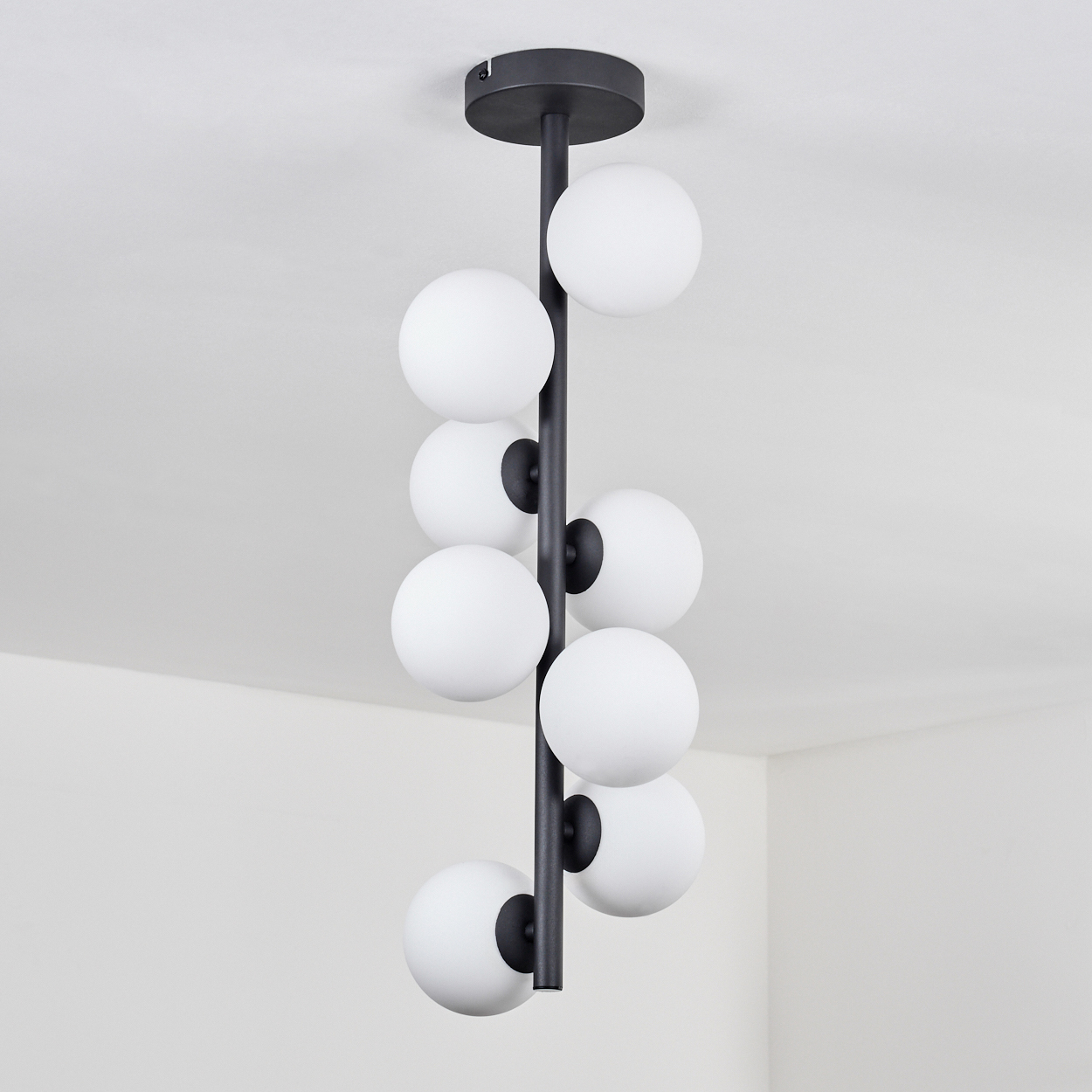 Eine schwarze, moderne Deckenleuchte mit weißen Kugelleuchten hängt von einer weißen Decke. Das Licht besteht aus acht Kugeln.