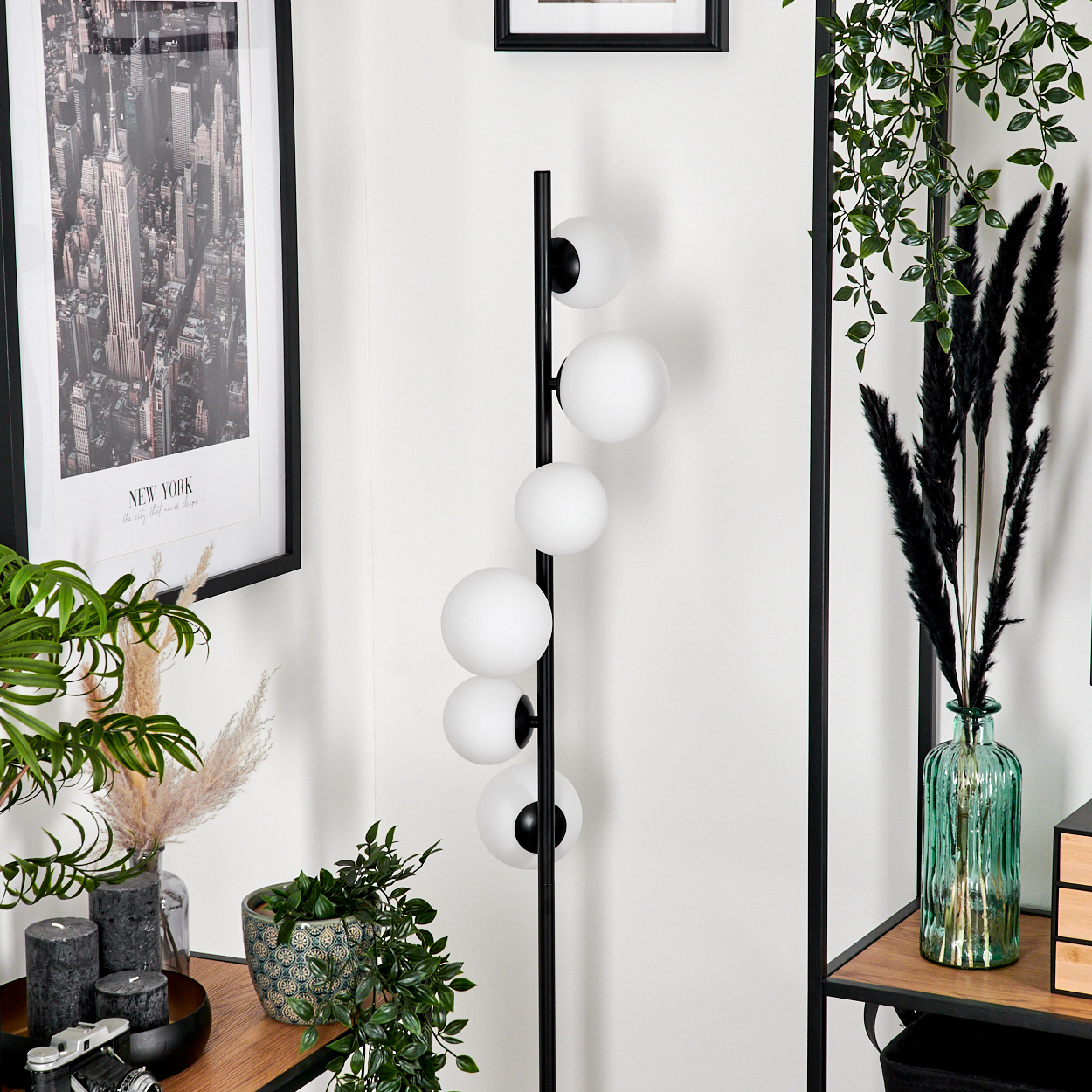 Zimmerecke mit Stehlampe und Dekoration. Ein New York-Stadtbild und eine grüne Vase mit schwarzem Ziergras sind ebenfalls vorhanden.