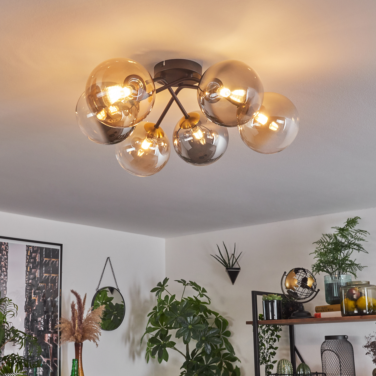 Deckenleuchte mit sieben kugelförmigen Lampen. Darunter ein Innenraum mit Pflanzen, einem Spiegel und Regalen mit Dekorationen.