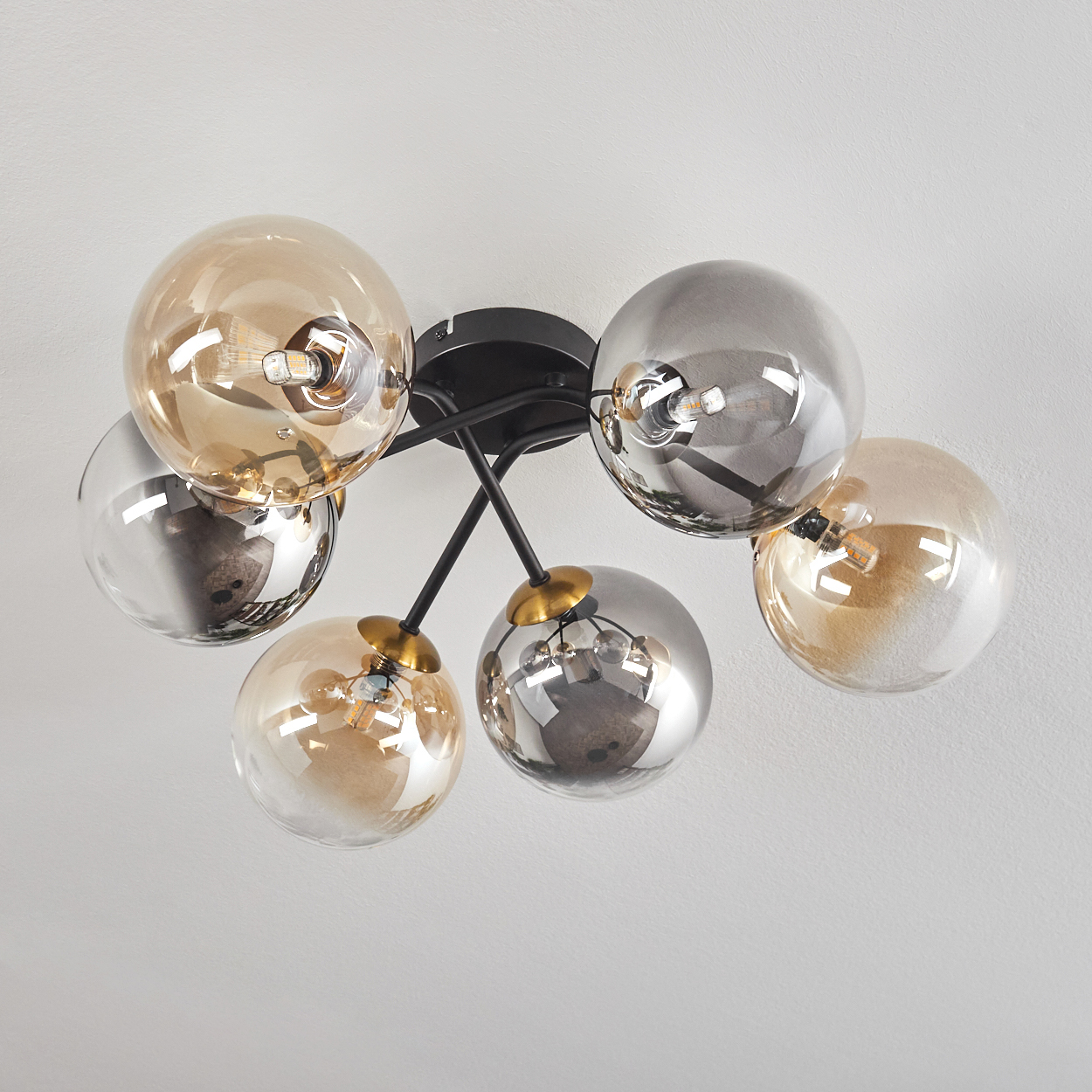 Eine moderne Deckenleuchte mit sechs kugelförmigen Glasschirmen in Silber und Bernstein, befestigt an schwarzen Metallarmen.
