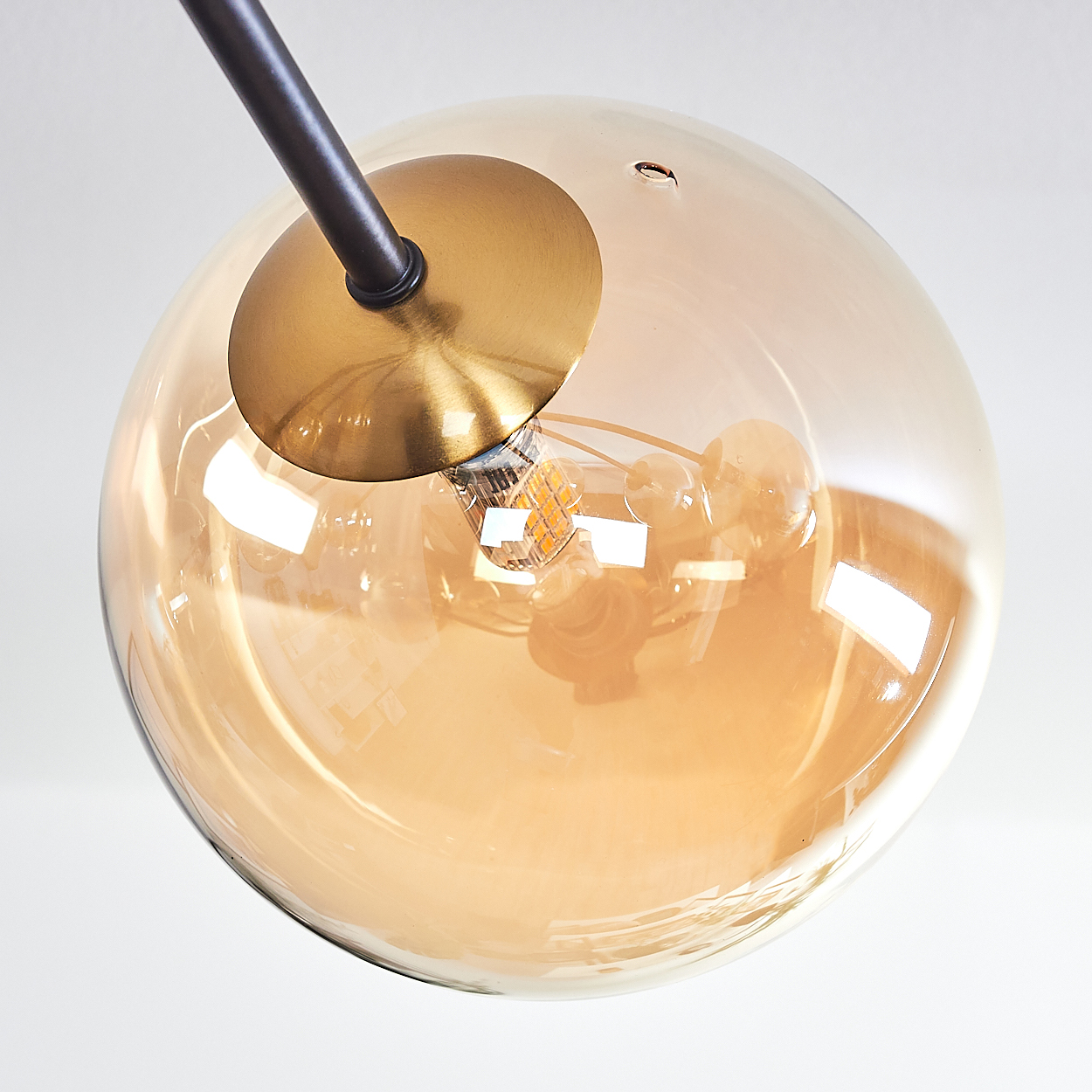 Nahaufnahme einer modernen Leuchte. Eine braune Metallstange trägt einen runden, bernsteinfarbenen Glaskörper mit Glühbirne und Messingdetails.