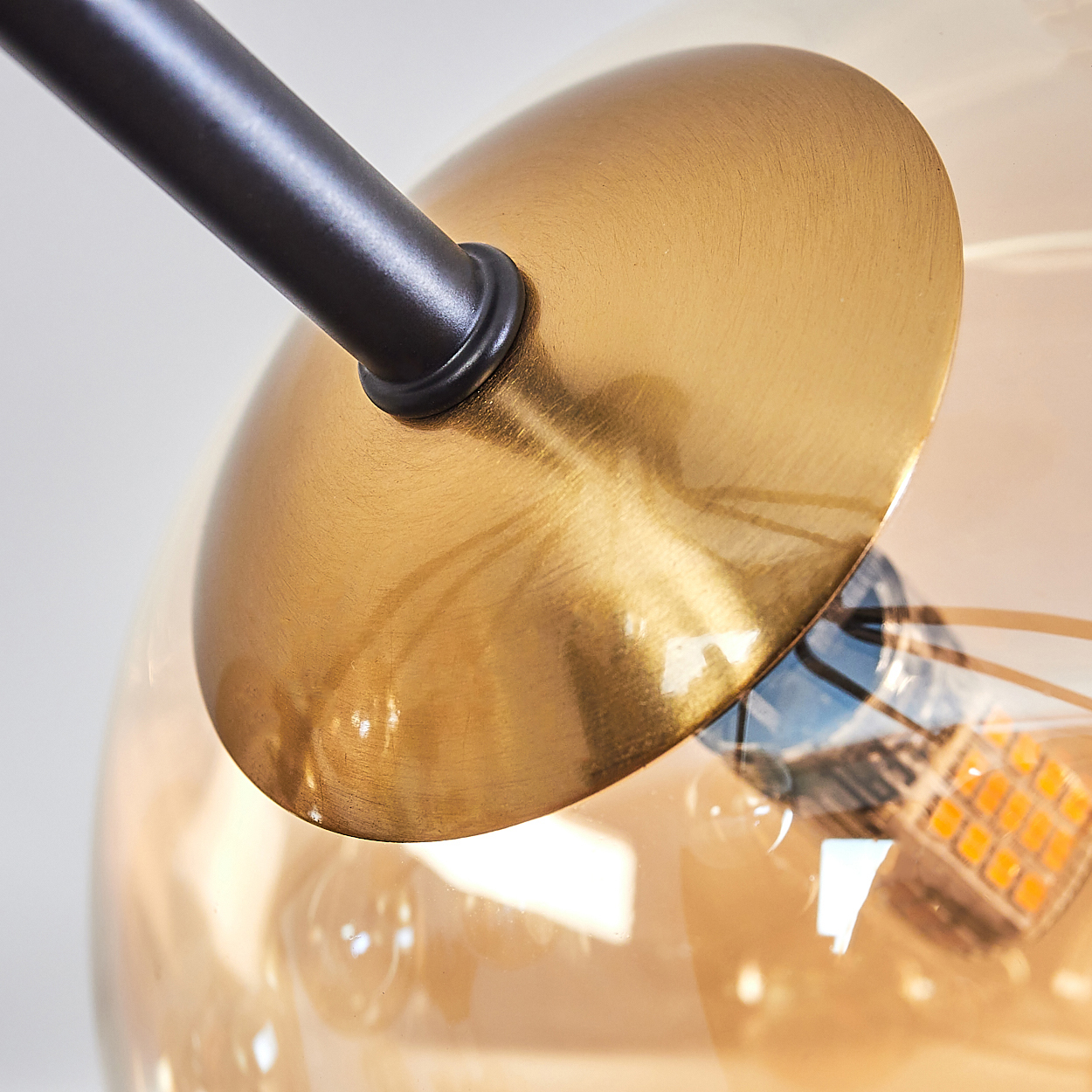 Nahaufnahme einer modernen Lampe. Ein goldfarbener Metallschirm bedeckt die Glühbirne, die an einer schwarzen Metallstange befestigt ist.