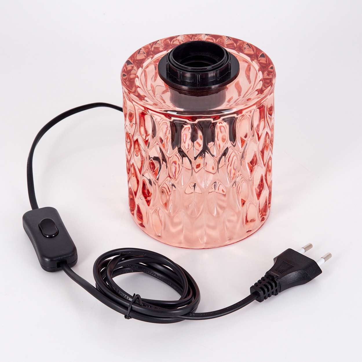 Eine roségoldene Glaslampe mit schwarzem Besatz und einem schwarzen Netzkabel mit Schalter und Stecker auf weißer Oberfläche.