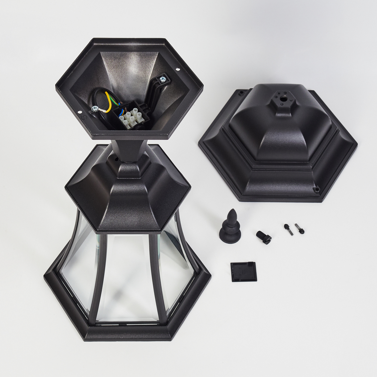 Zerlegte schwarze Außenlampe auf Weiß. Teile umfassen Basis, Oberteil, Glasscheiben und elektrische Komponenten. Schrauben und Kleinteile sind sichtbar.