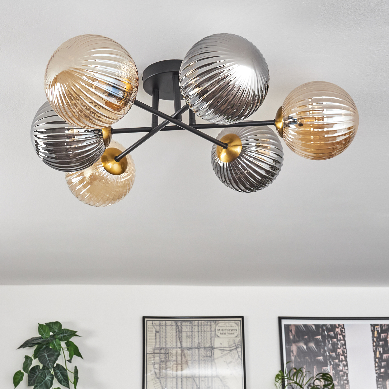 Eine moderne Deckenleuchte mit sechs Glasglobus in Gold und Silber, angeordnet auf schwarzen Metallarmen, vor weißer Decke.
