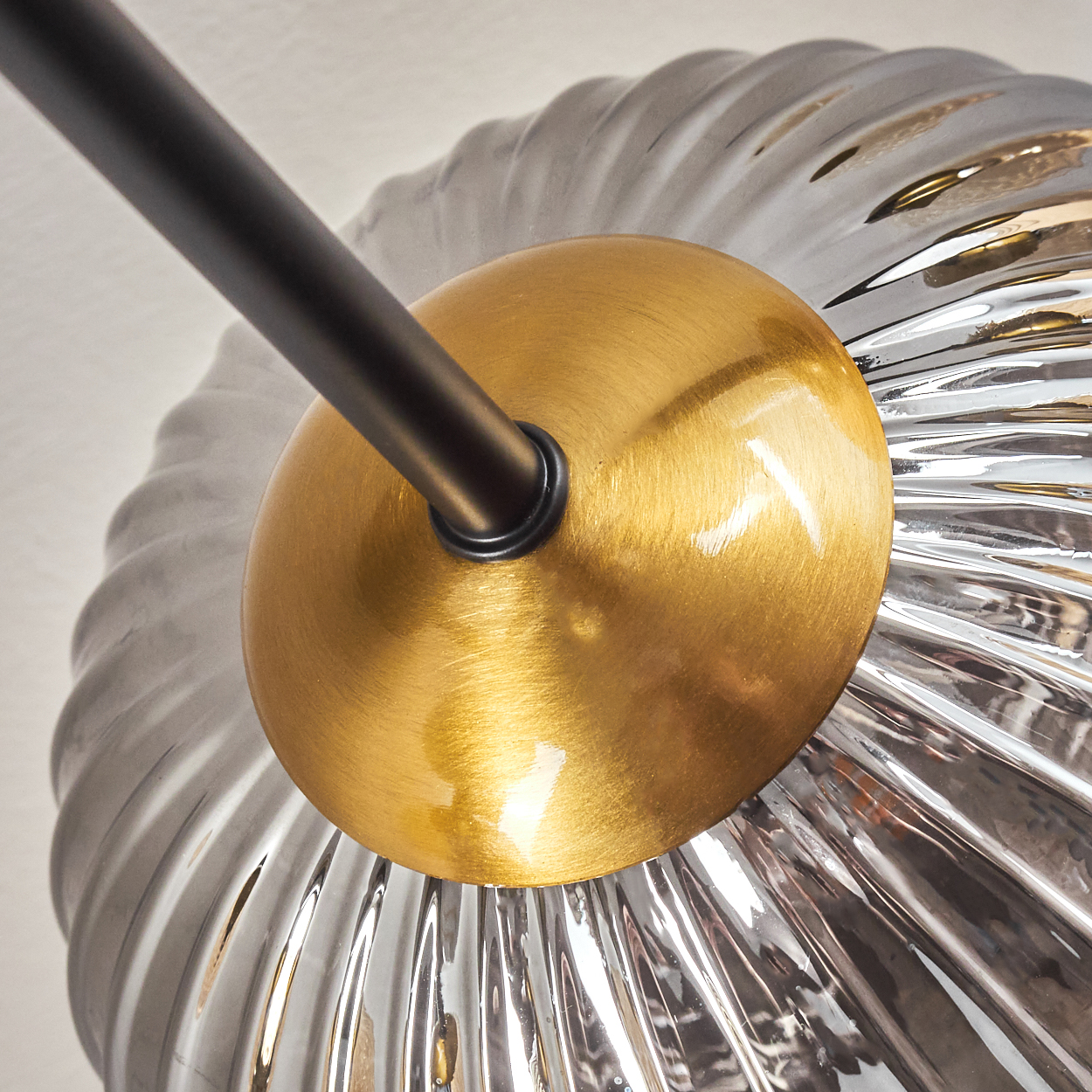 Nahaufnahme einer modernen Leuchte mit goldenem Sockel, schwarzem Arm und klarem, geriffeltem Glasschirm.