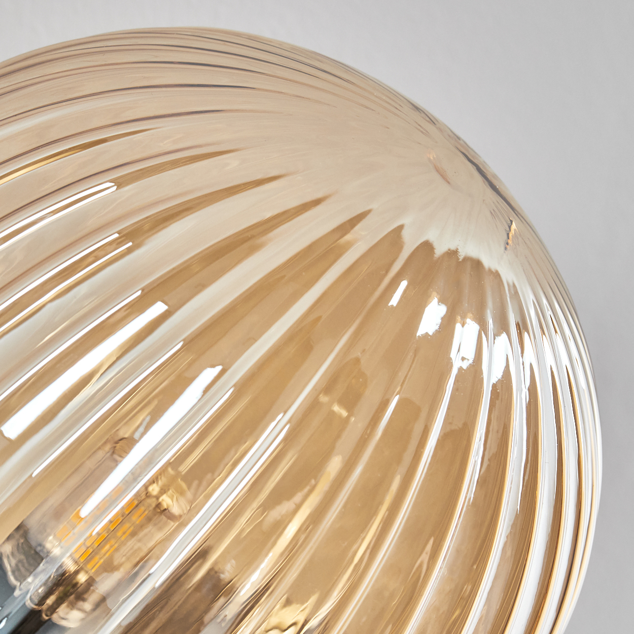 Nahaufnahme einer Leuchte. Der Glasschirm ist bernsteinfarben mit einem Spiraldesign. Das Licht ist an, und der Hintergrund ist weiß.