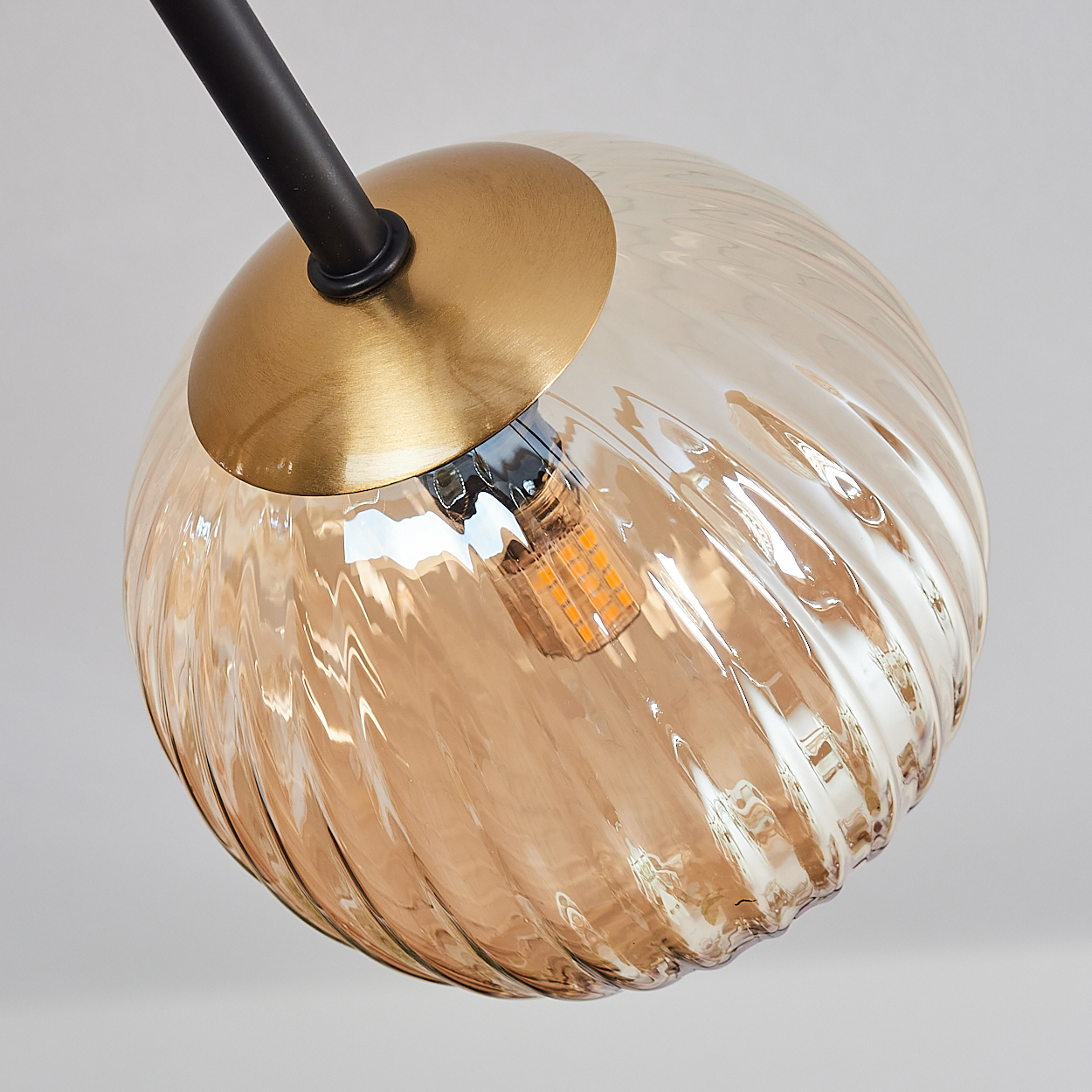 Nahaufnahme einer Leuchte mit einem strukturierten Glaskolben. Der Globus ist bernsteinfarben mit goldfarbenem Sockel. Eine schwarze Stange stützt ihn.