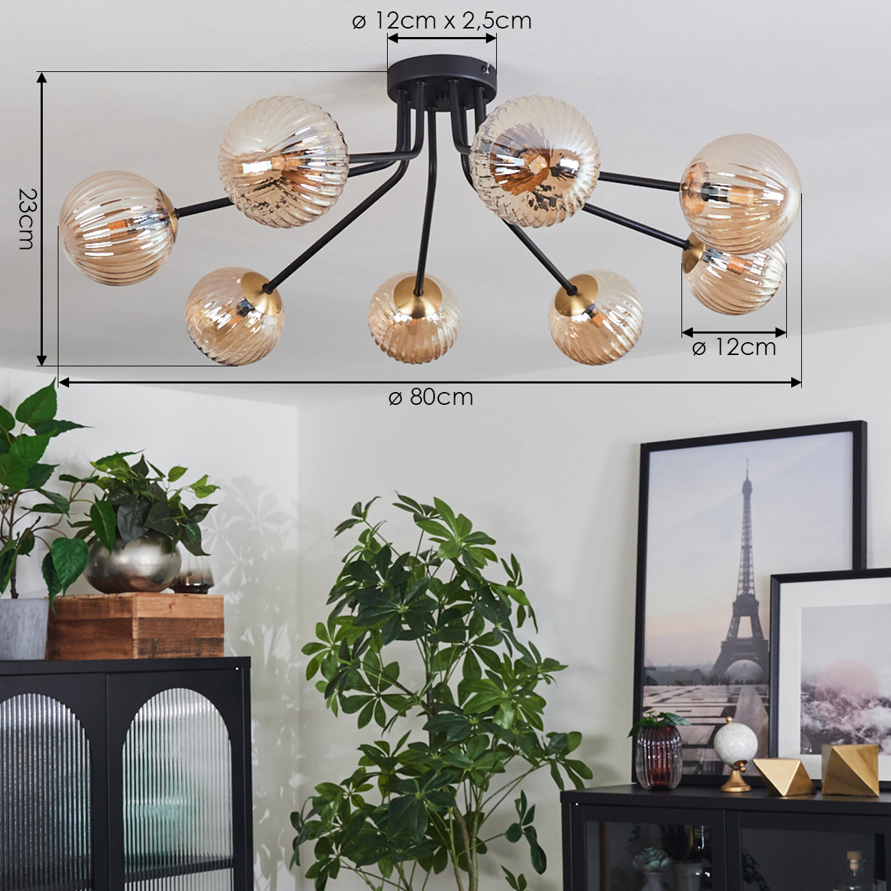 Deckenlampe mit Glaskugeln, schwarzen Armen und goldenen Akzenten. Grüne Pflanzen und schwarze Möbel im Vordergrund. Eiffelturm sichtbar.