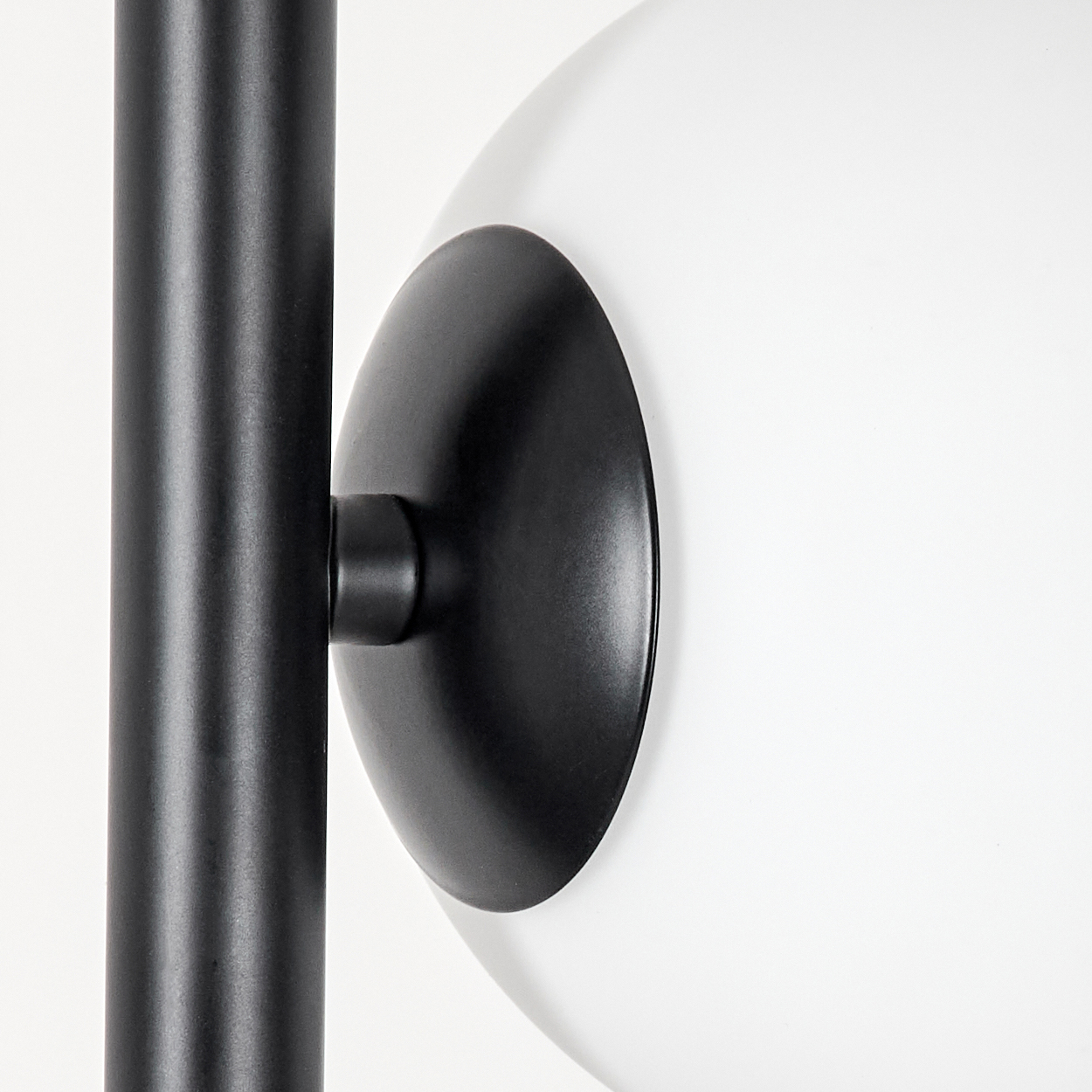 Nahaufnahme einer schwarzen Lampe mit rundem, weißem Glasschirm. Links ein schwarzer Pfosten. Der Hintergrund ist weiß.