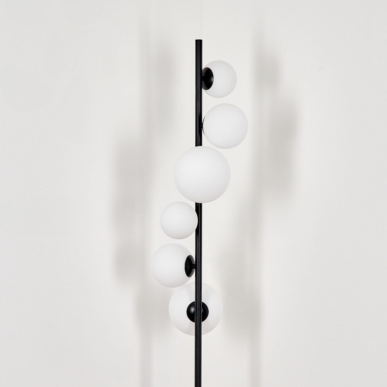 Eine moderne Lampe mit weißen Kugeln und einem schwarzen Pfahl. Die Kugeln sind vertikal angeordnet, mit einer weißen Wand im Hintergrund.
