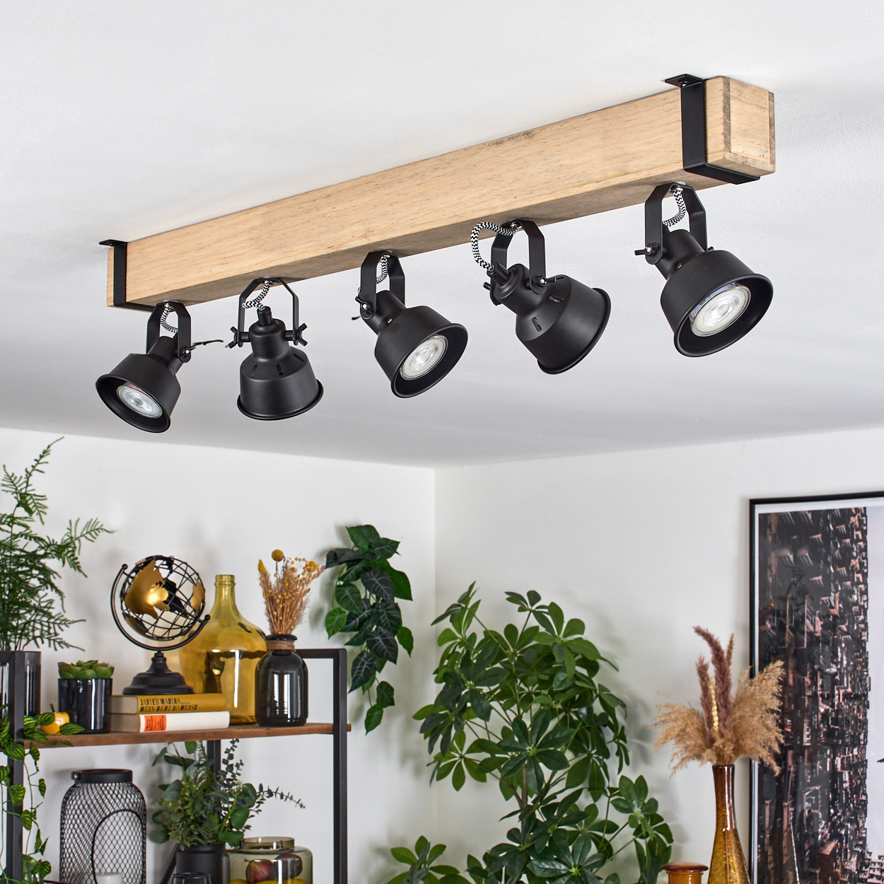 Schwarze Strahler an einem Holzbalken an einer weißen Decke. Darunter ein Regal mit Pflanzen, Globus und Dekoration.