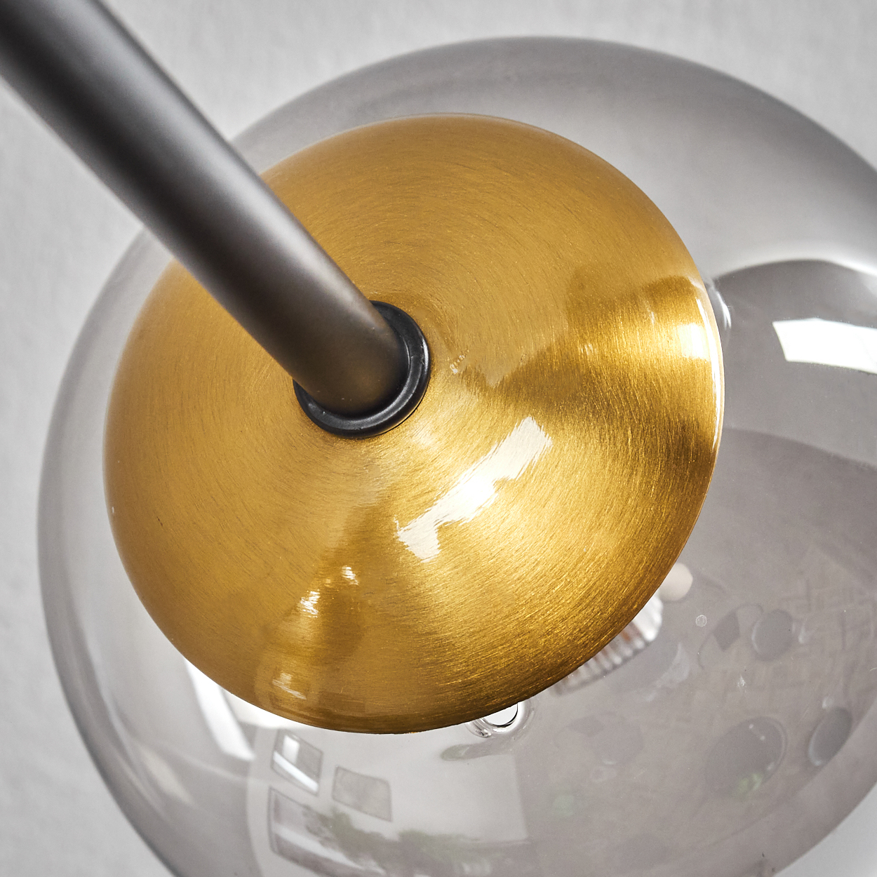 Nahaufnahme einer modernen Leuchte mit goldfarbener Scheibe, grauer Glaskugel und dunklem Arm.