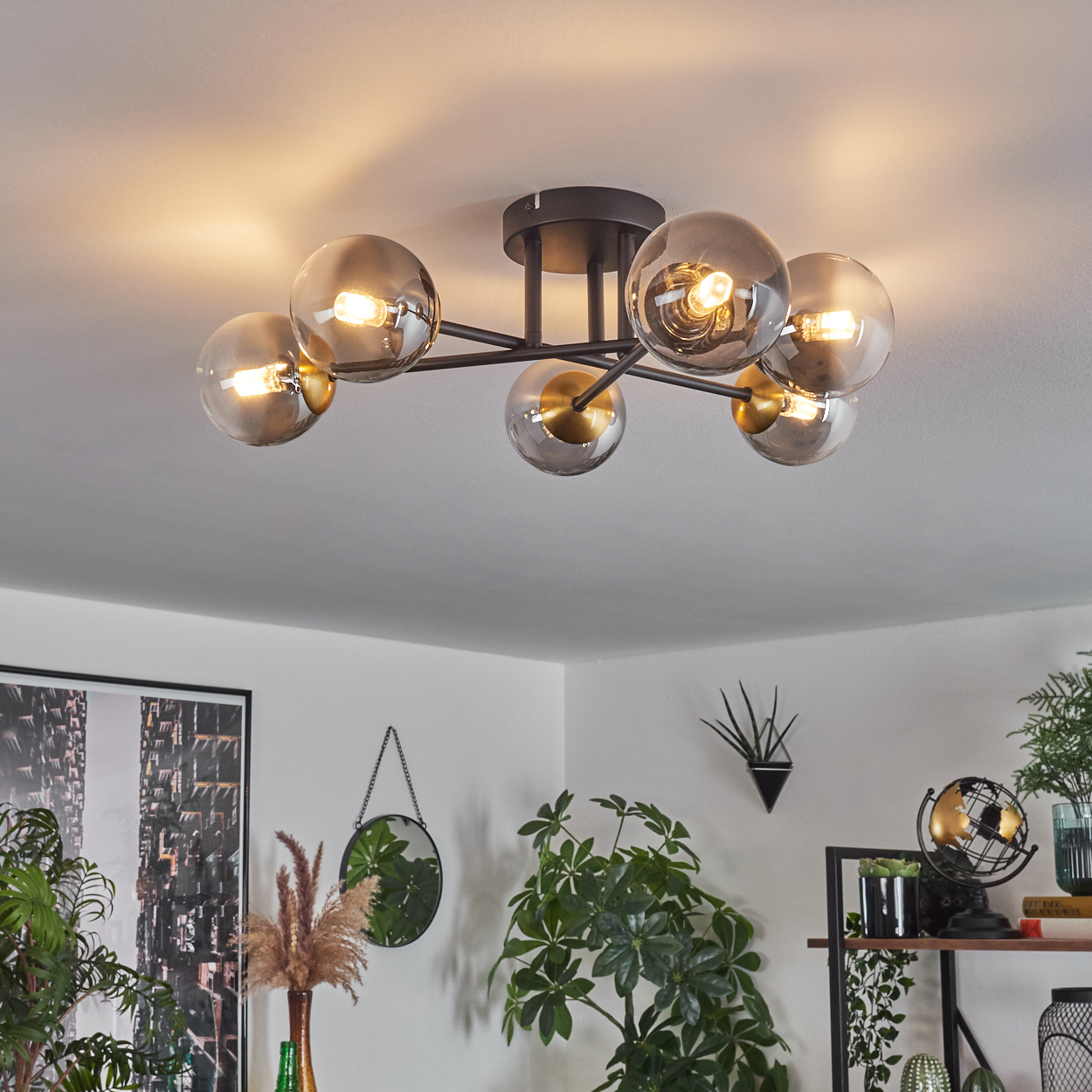 Deckenleuchte mit sechs Glaskugeln. Darunter Pflanzen, ein Spiegel und ein Globus schmücken den Raum. Das Licht ist an.