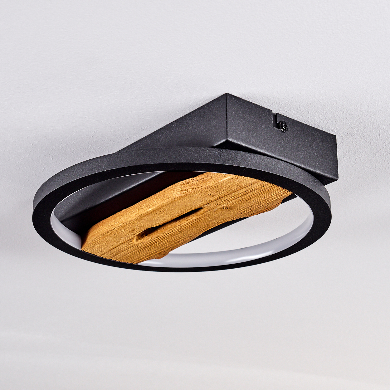 Eine schwarze Deckenleuchte mit einem Holzteil. Die Lampe hat ein kreisförmiges Design mit Licht und ist an der Decke befestigt.
