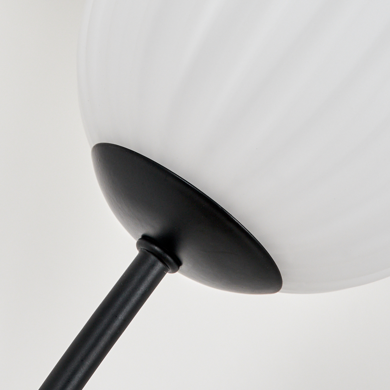 Nahaufnahme einer Lampe. Ein weißer, runder Lampenschirm befindet sich über einer schwarzen, gebogenen Metallstütze. Der Hintergrund ist weiß.
