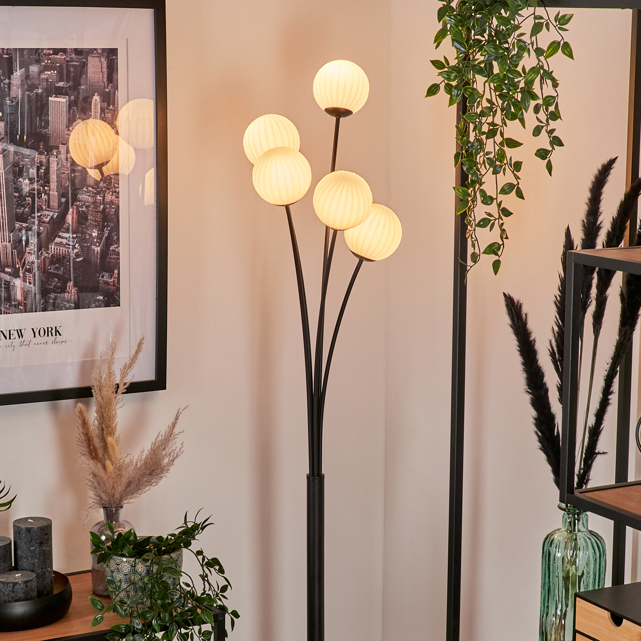 Eine Stehlampe mit fünf Kugelleuchten. Ein New York-Stadtbild, Pflanzen und ein Regal sind ebenfalls im Raum zu sehen.