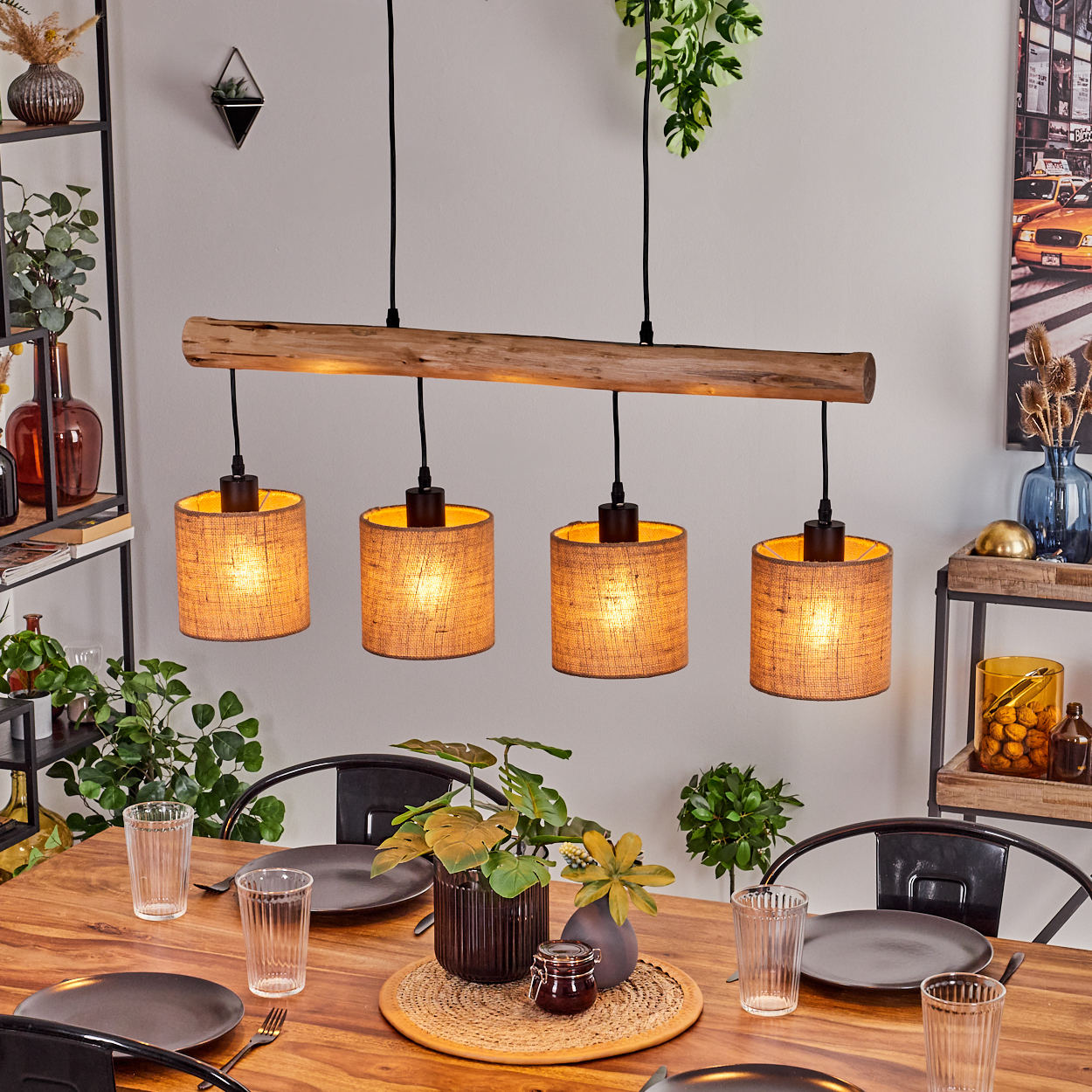 Esstisch mit vier Pendelleuchten. Ein Holzbalken hält die Lampenschirme. Tisch gedeckt mit Tellern, Gläsern und Pflanzen. Hintergrund mit Regalen.
