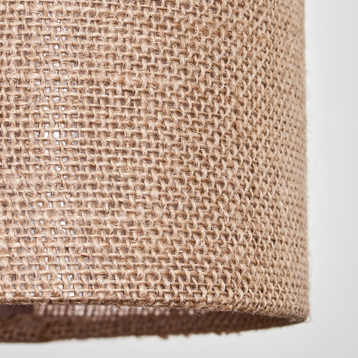 Nahaufnahme eines beigefarbenen Lampenschirms aus Jute mit gewebter Textur. Der Hintergrund ist eine schlichte weiße Oberfläche.