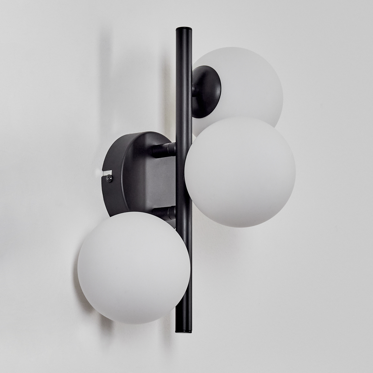 Eine moderne Wandlampe mit schwarzem Rahmen und drei weißen Kugelleuchten an einer weißen Wand.