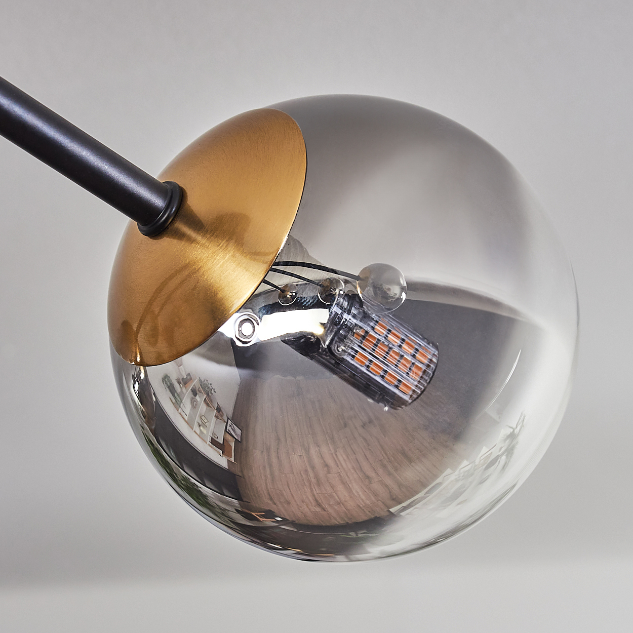 Eine moderne Lampe mit einer Glaskugel, Goldakzent und schwarzem Arm. Die Kugel spiegelt einen Raum. Eine orangefarbene LED ist sichtbar.