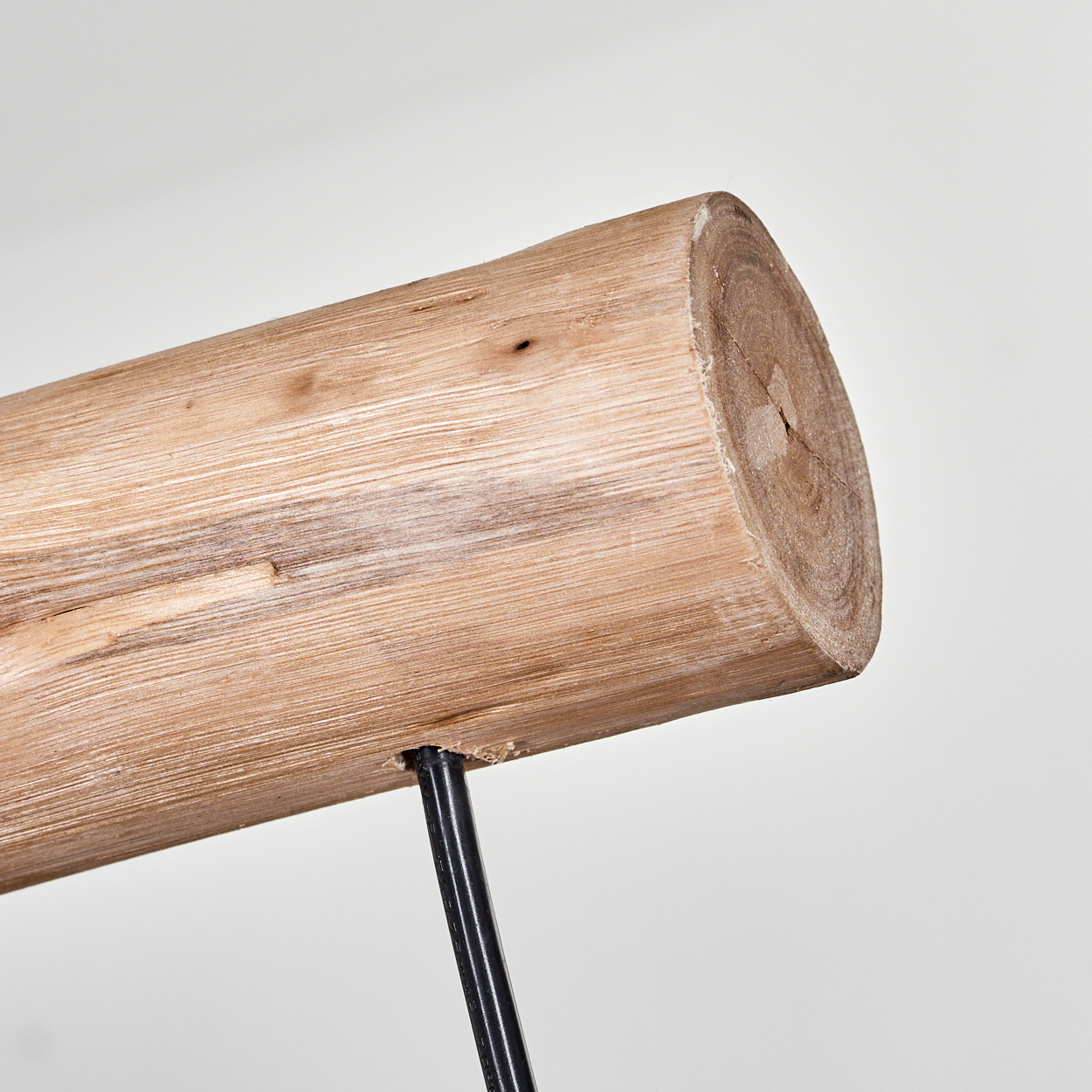 Nahaufnahme eines Holzstamms, der von einem schwarzen Metallbein getragen wird. Der Stamm ist hellbraun mit sichtbarer Maserung. Der Hintergrund ist weiß.
