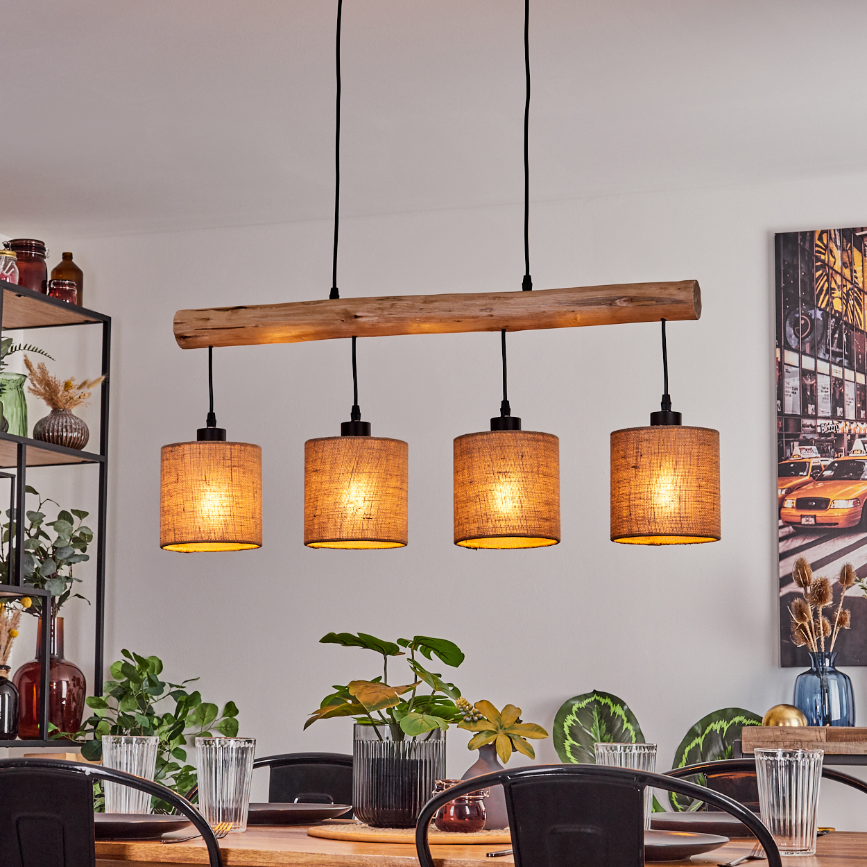 Ein Esszimmer mit einer Holzbalken-Leuchte mit vier Lampen. Ein Gemälde befindet sich an der Wand. Vorne steht ein Tisch mit Gläsern und Pflanzen.