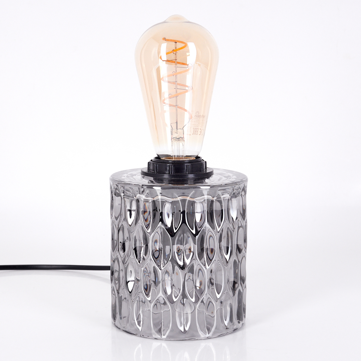 Eine dekorative Tischlampe mit einer großen, warm getönten Glühbirne und einem strukturierten, zylindrischen Sockel. Der Hintergrund ist weiß.