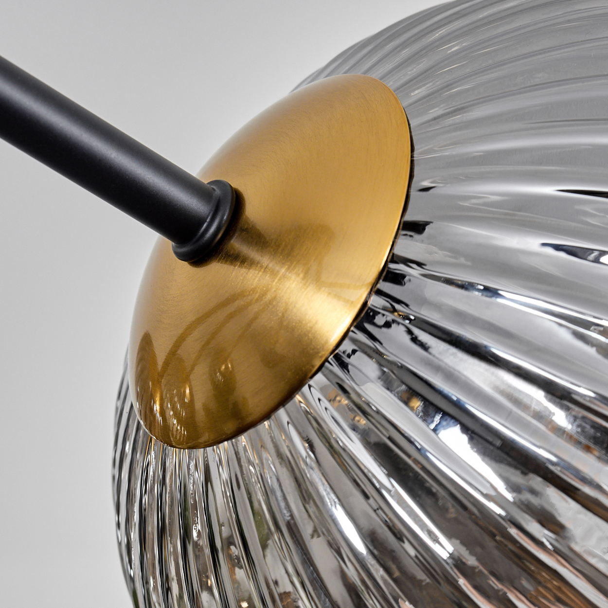 Nahaufnahme einer modernen Lampe. Sie hat einen goldfarbenen Sockel, einen schwarzen Arm und einen strukturierten, transparenten Glasschirm.