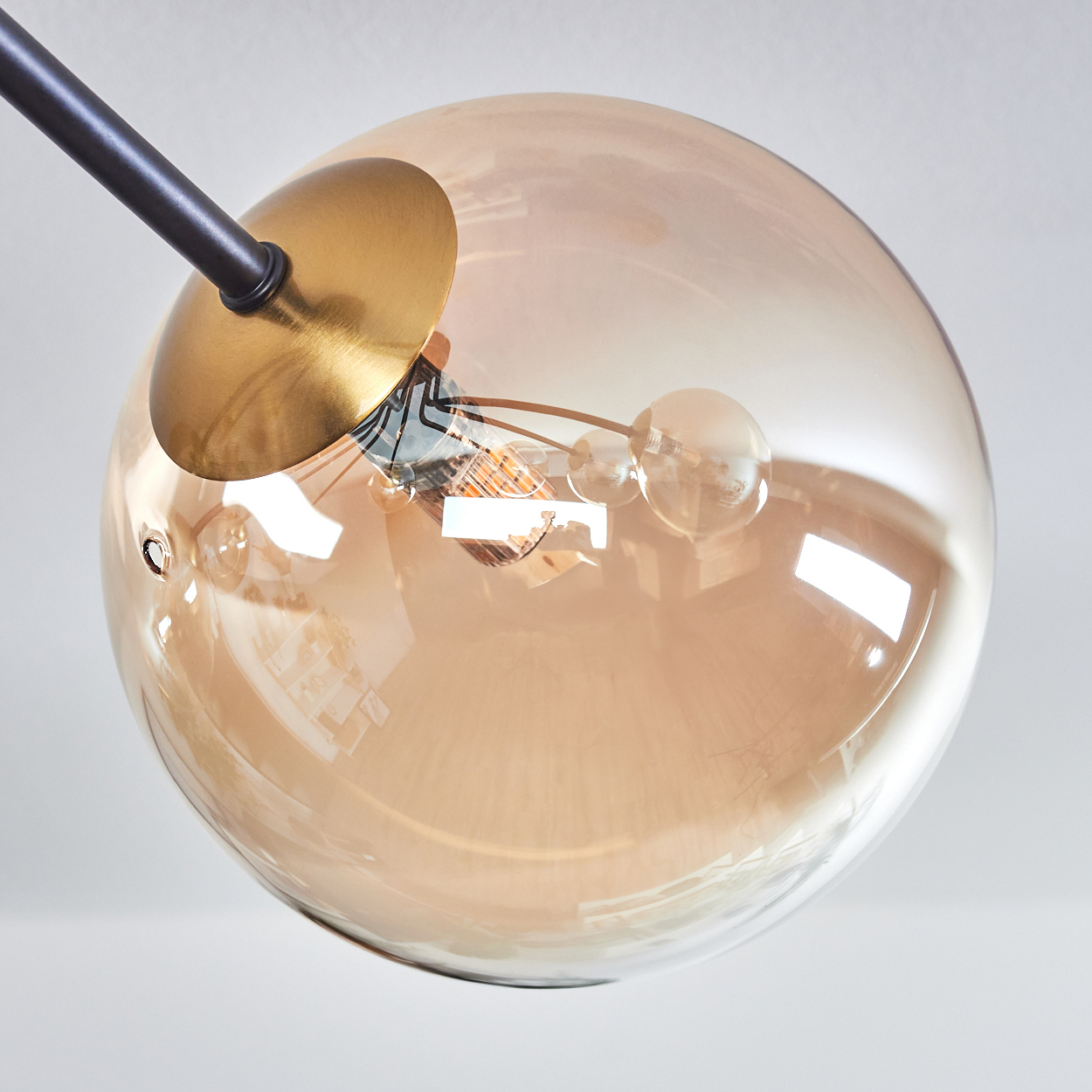 Nahaufnahme einer modernen Pendelleuchte mit einer großen, bernsteinfarbenen Glaskugel und einem schwarzen Metallarm.