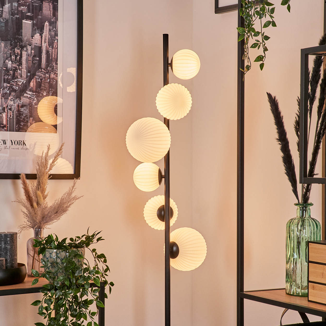 Eine moderne Stehlampe mit sechs leuchtenden Kugeln. Pflanzen, ein Stadtplakat und Dekorationsartikel im Hintergrund.