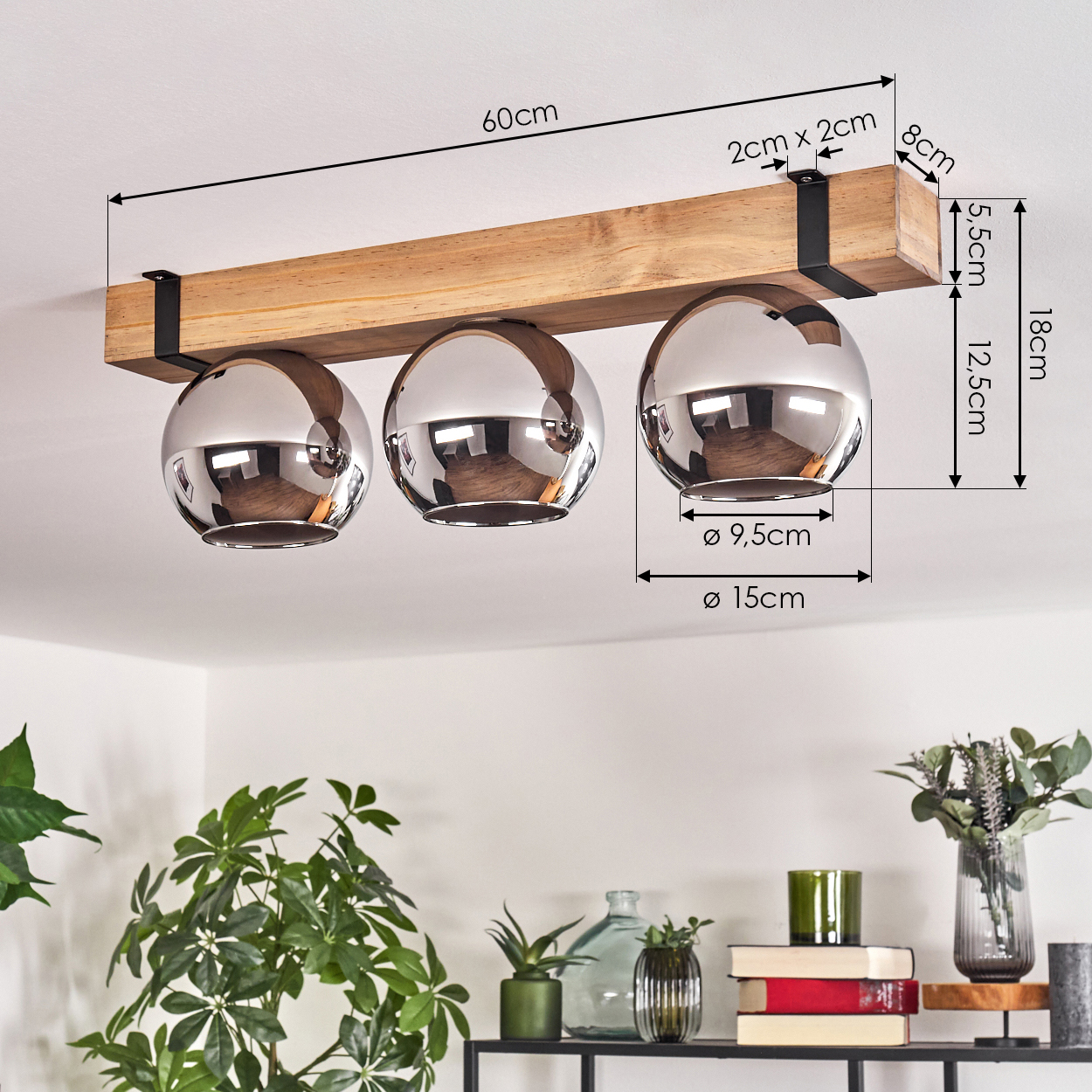 Ein Holzbalken mit drei silbernen, kugelförmigen Lampen ist an der Decke befestigt. Darunter stehen Pflanzen und Dekorationsartikel auf einem Regal.