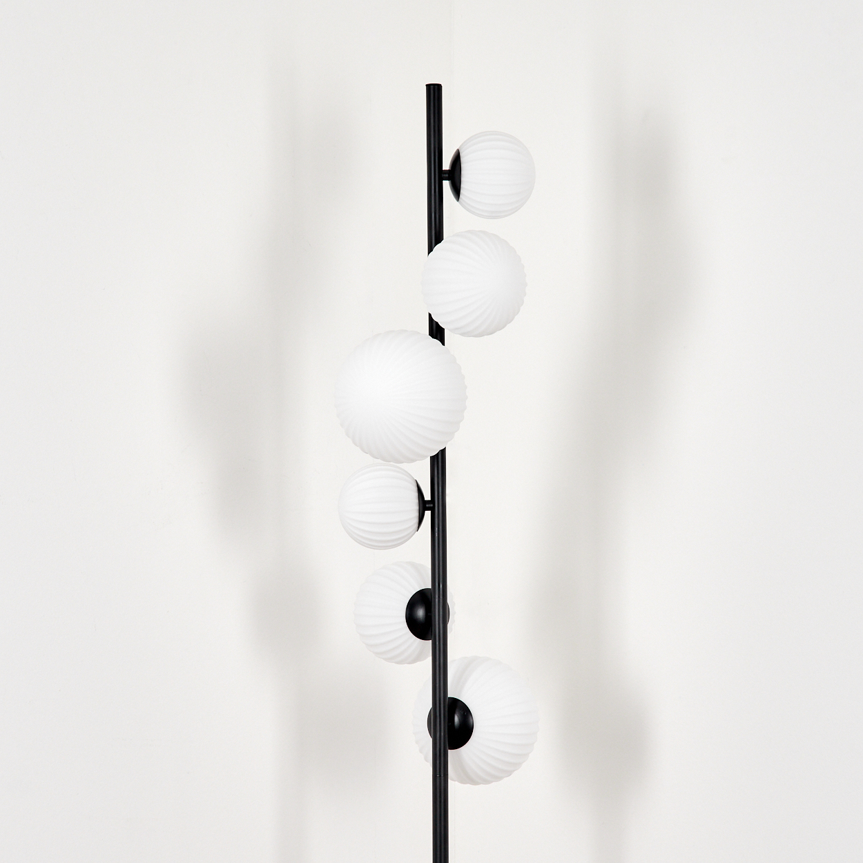 Eine moderne Stehlampe mit sechs weißen, kugelförmigen Lichtern. Die Lampe ist schwarz, mit einem vertikalen Pfosten und gebogenen Armen.