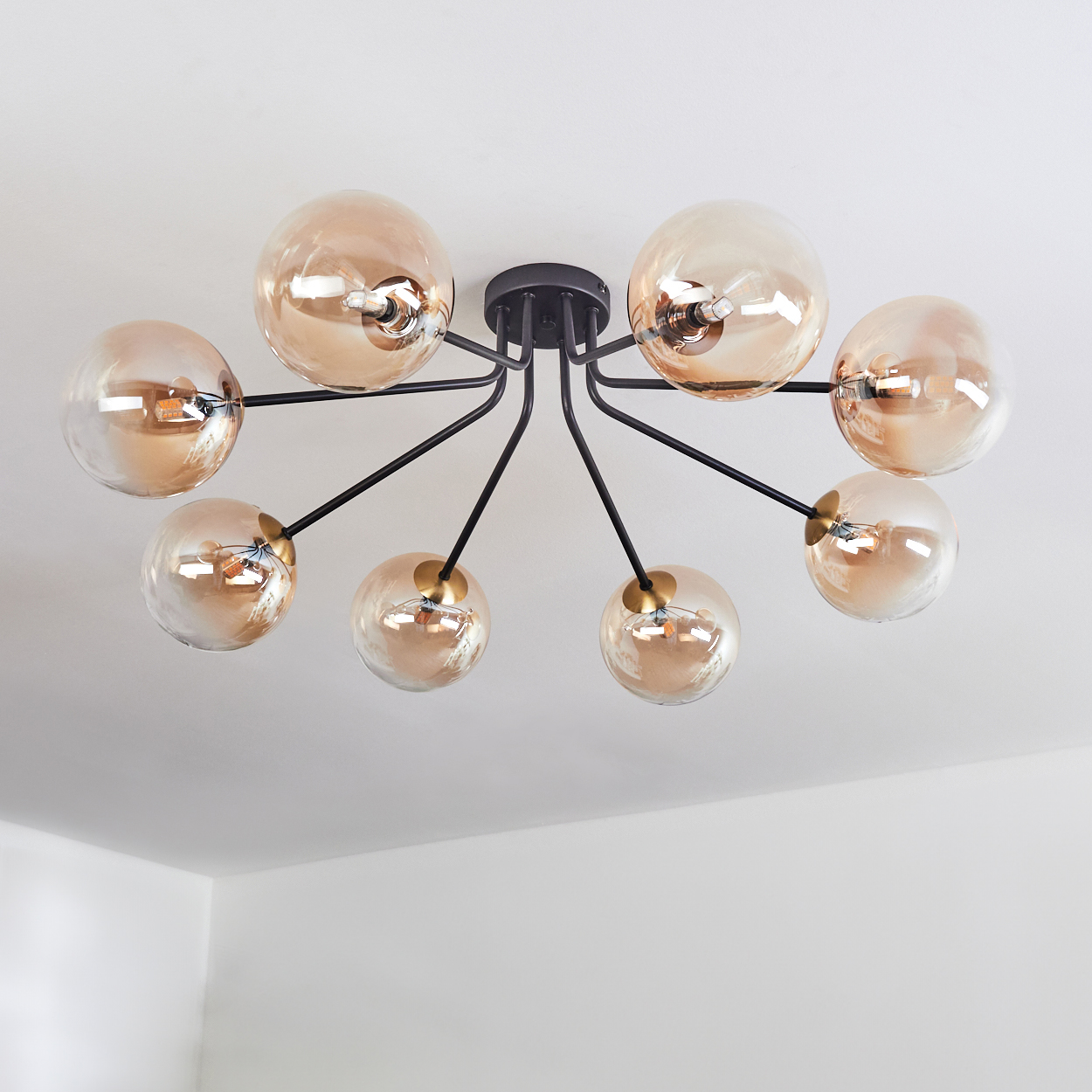 Eine moderne Deckenleuchte mit acht bernsteinfarbenen Glaskugeln und schwarzen Armen, an einer weißen Decke befestigt.